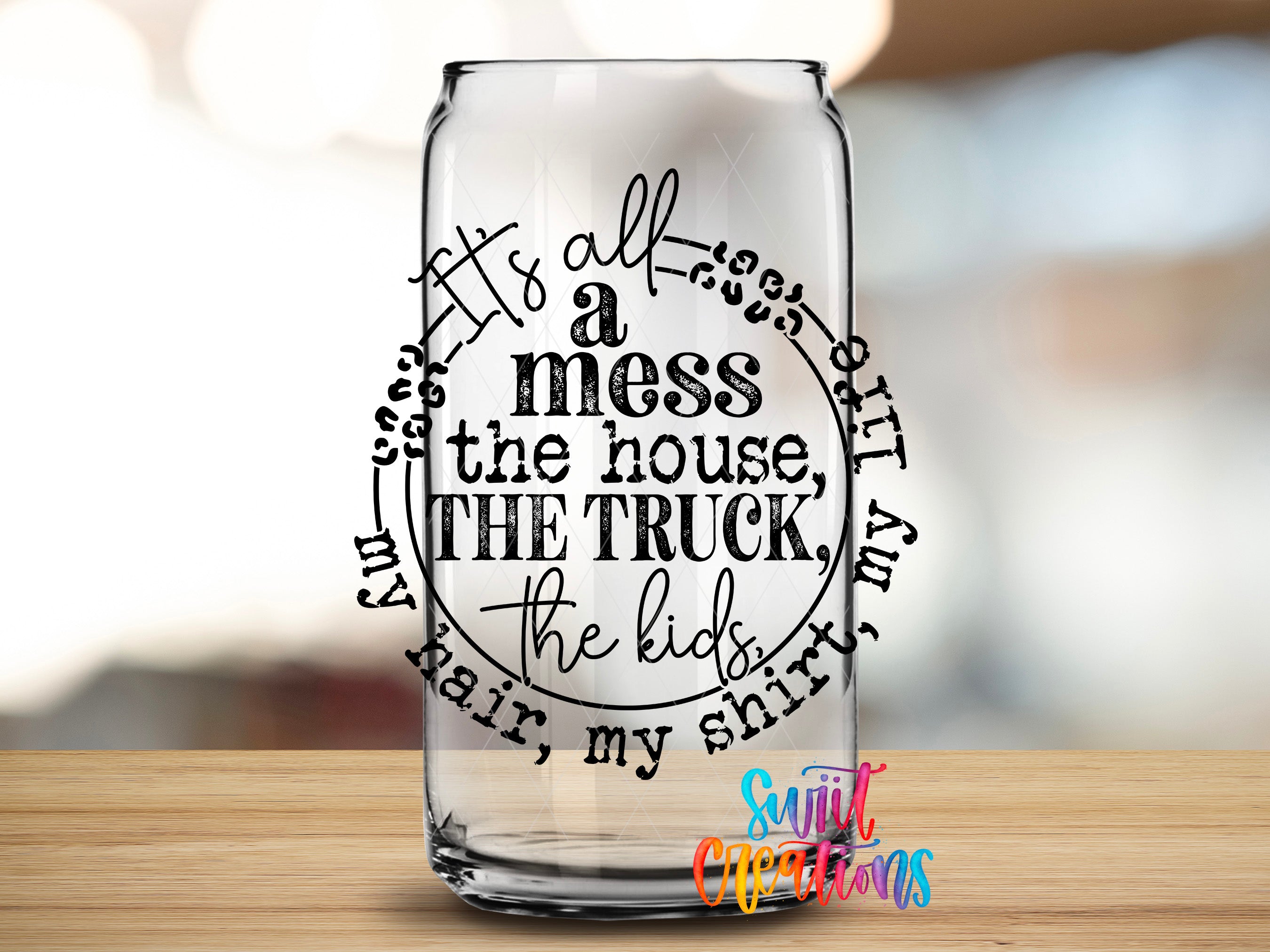 A clear glass can with a hand-lettered quote printed on it, placed on a wooden surface.