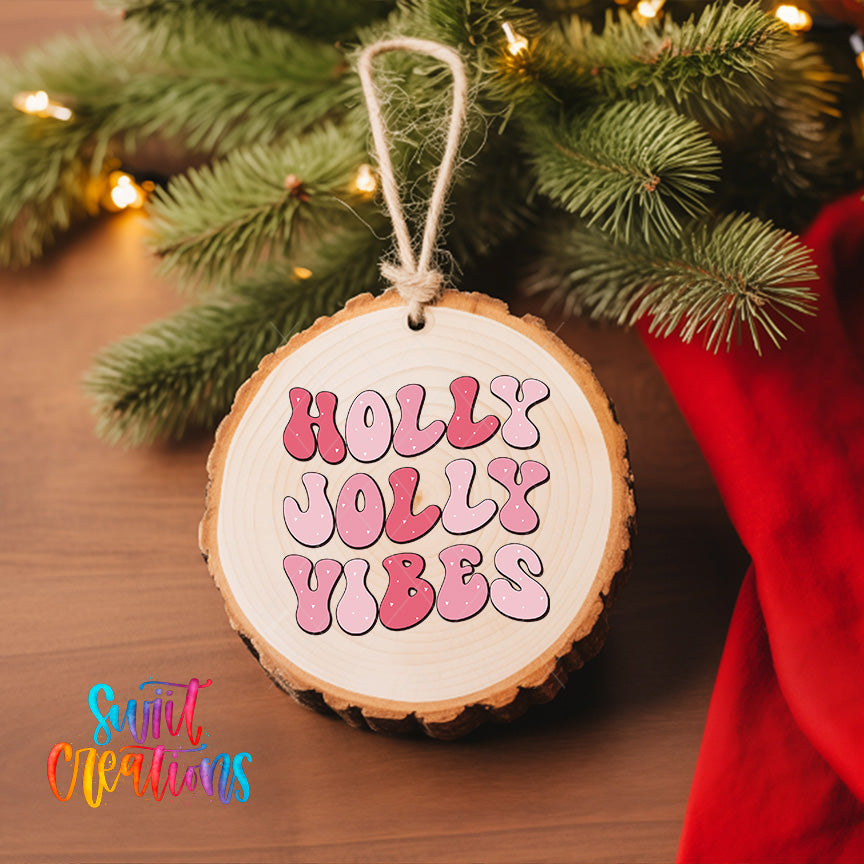 A wooden ornament with the text "HOLY JOYLY VIBES" hanging from a tree branch, surrounded by pine branches and twinkling lights.