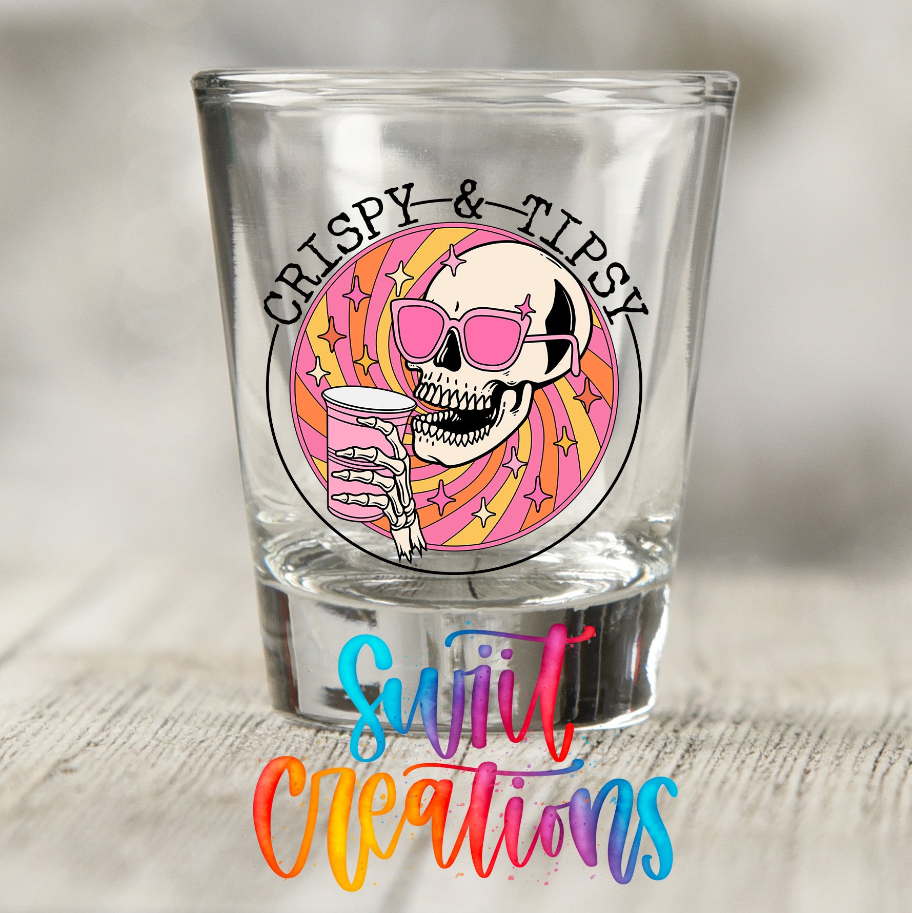 A shot glass with a skull wearing sunglasses and holding a drink, surrounded by a colorful, abstract design.