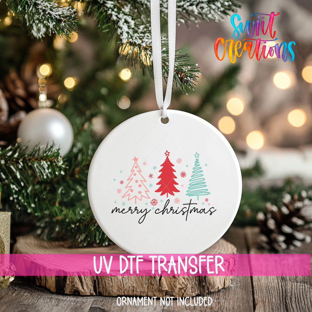 A white Christmas ornament with a design of three Christmas trees and the text "Merry Christmas" is hanging on a tree branch.