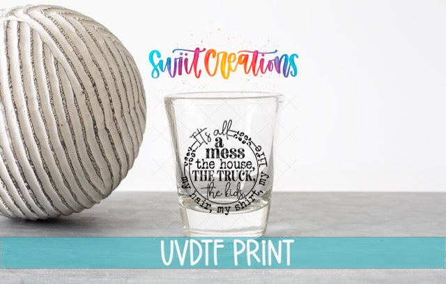 a shot glass with a message on it, placed next to a white ball on a gray surface.