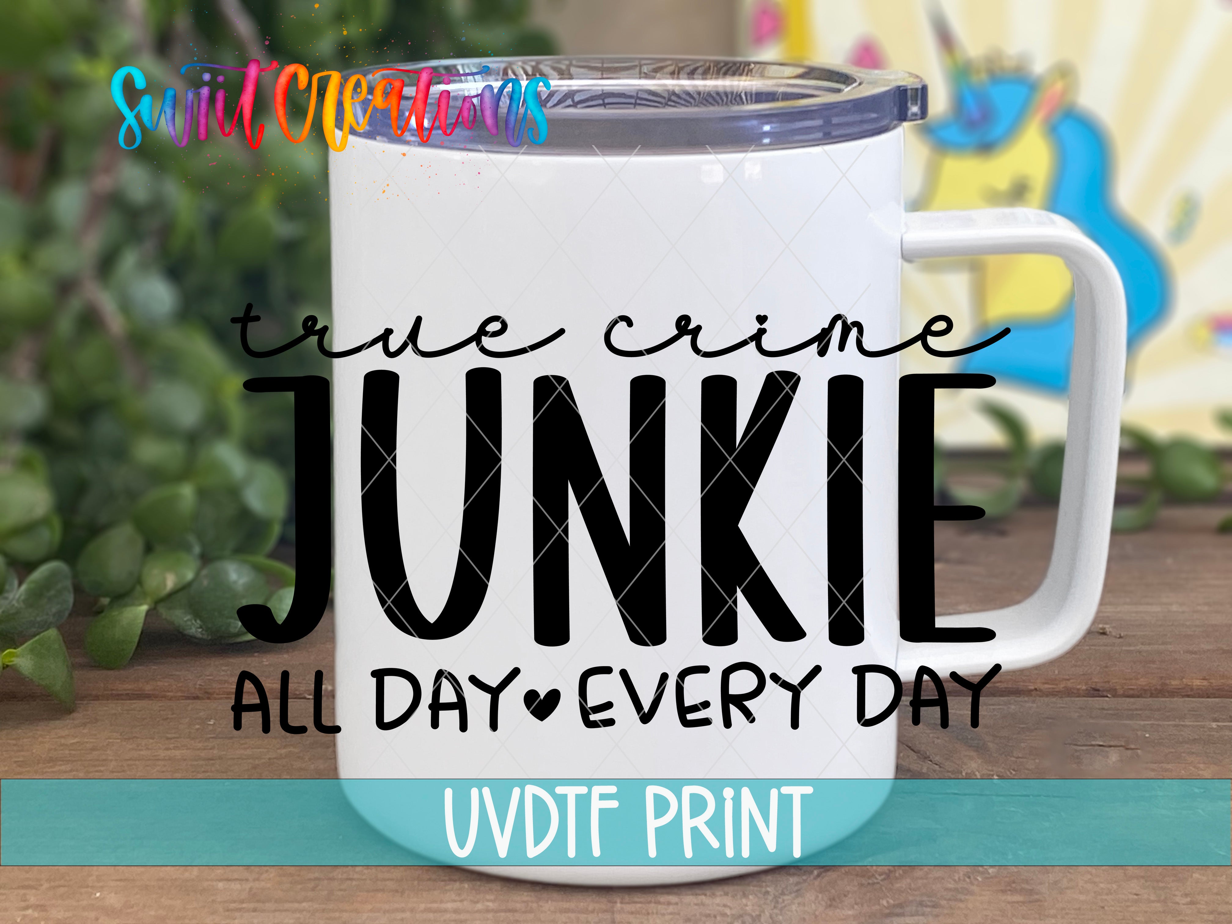 A white mug with a printed text design on it, placed on a wooden surface with greenery in the background.