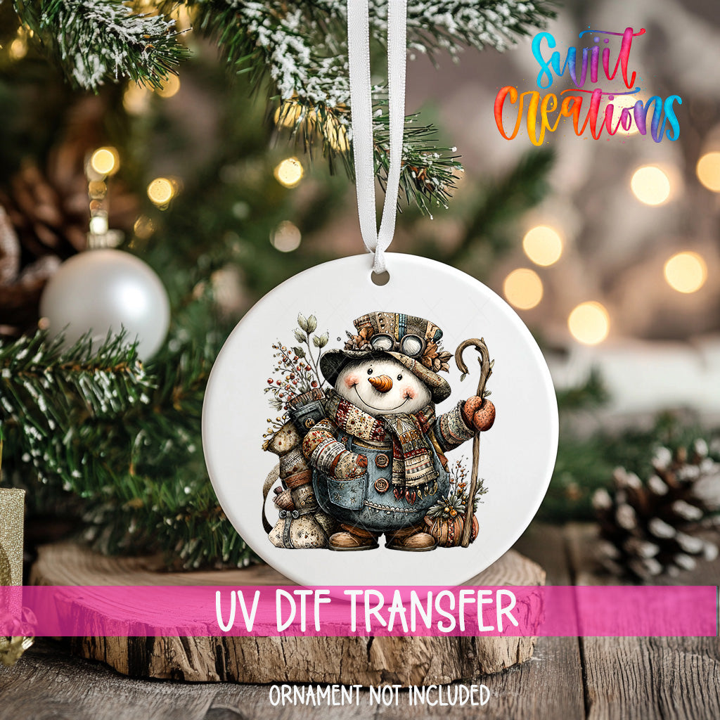 A white ornament with a snowman design hangs on a Christmas tree, surrounded by pine branches and other holiday decorations.