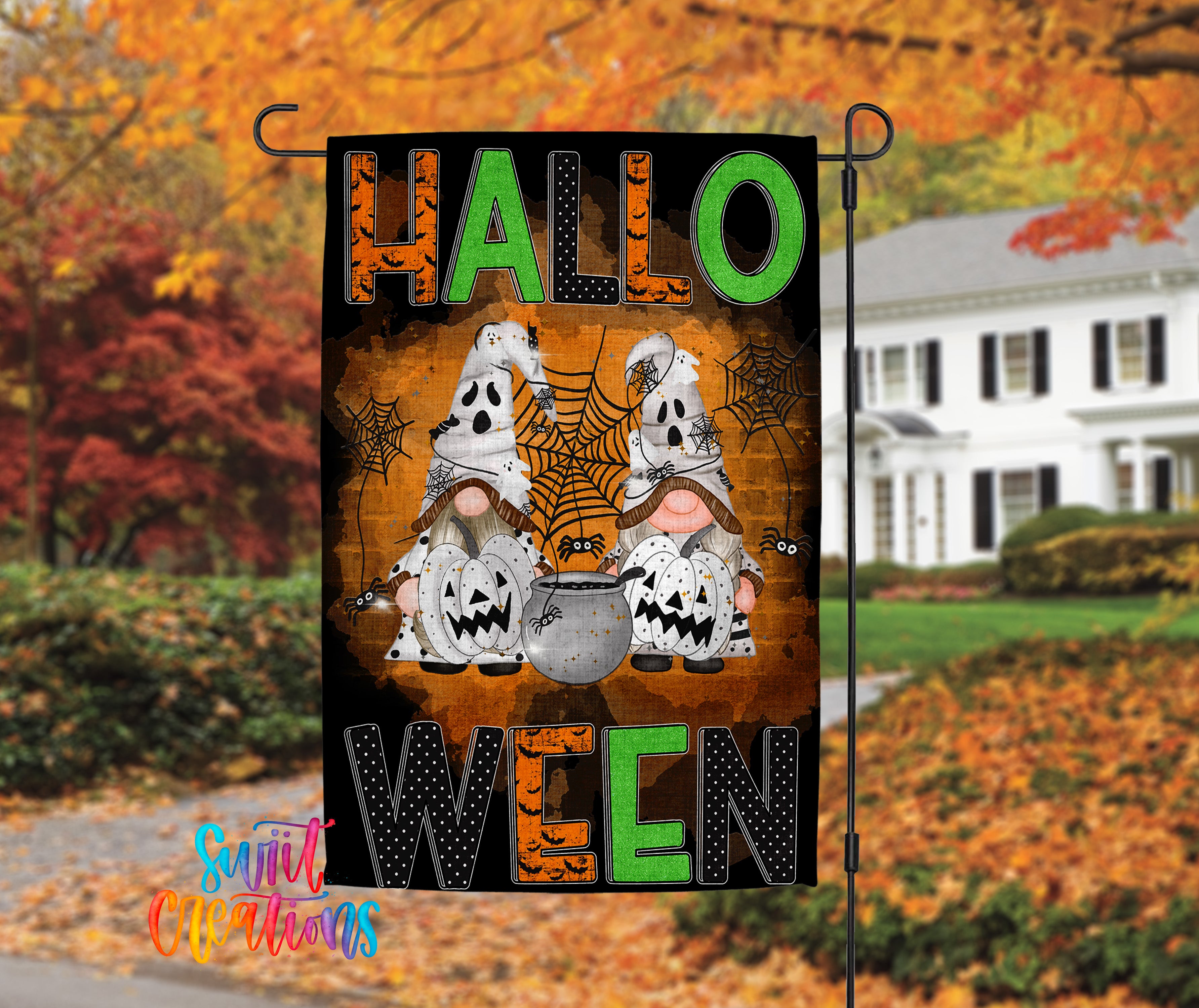 A Halloween-themed garden flag with two ghostly gnomes and a spider web, set against a backdrop of autumn foliage.