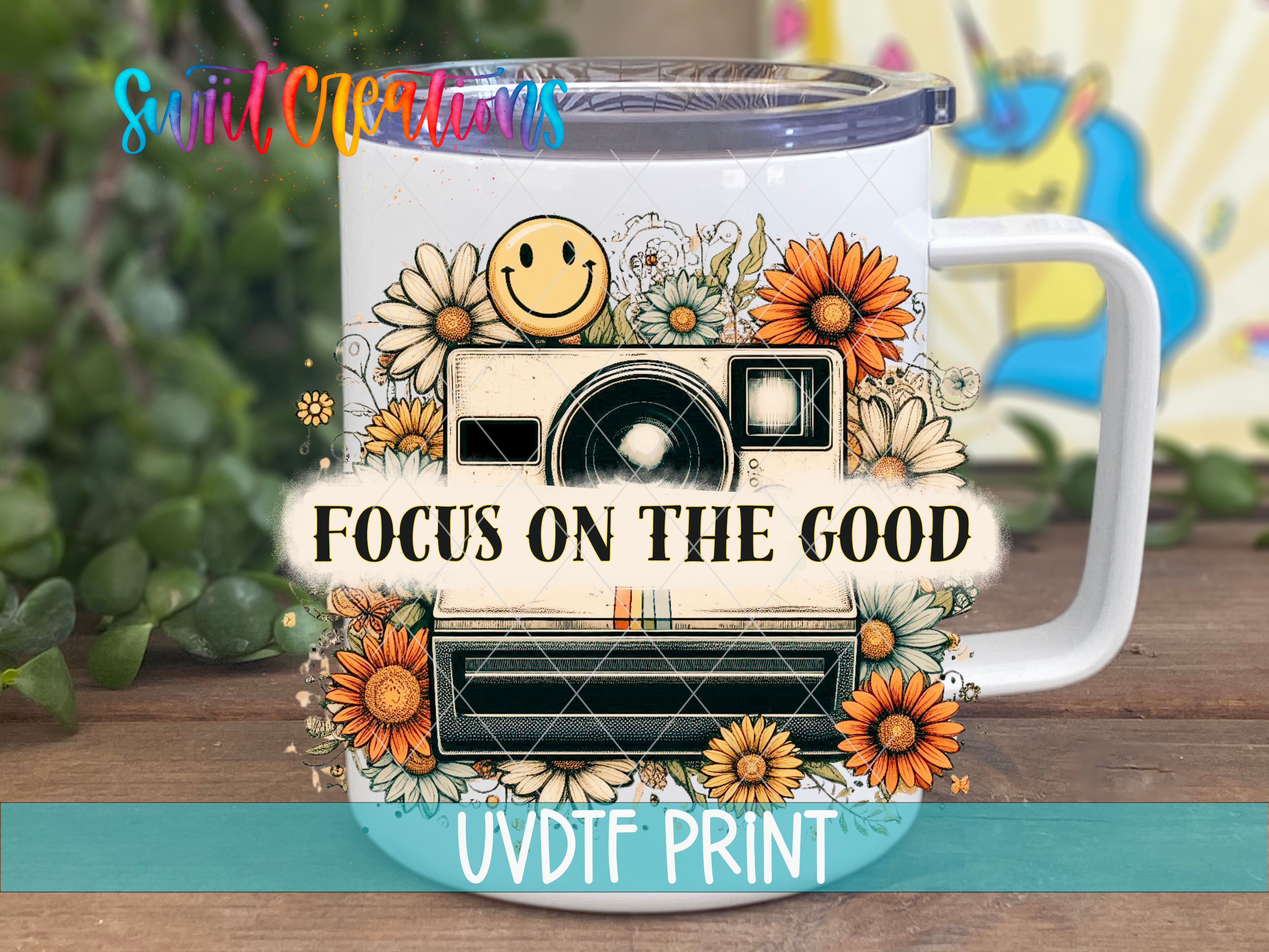 A white mug with a floral design and a camera, along with the text "Focus on the good" printed on it.