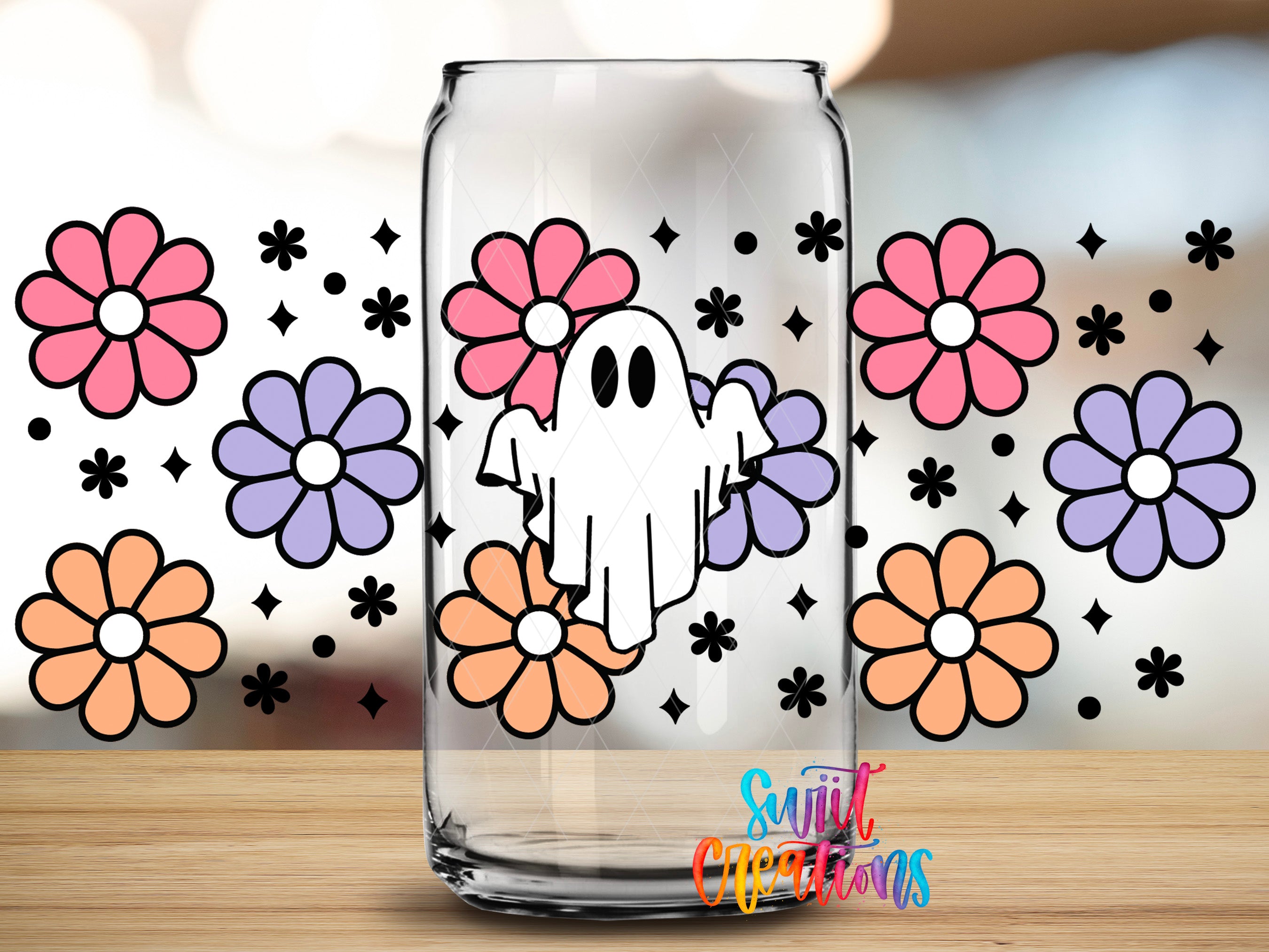 A clear glass can with a ghost design and colorful flowers printed on it, placed on a wooden surface.