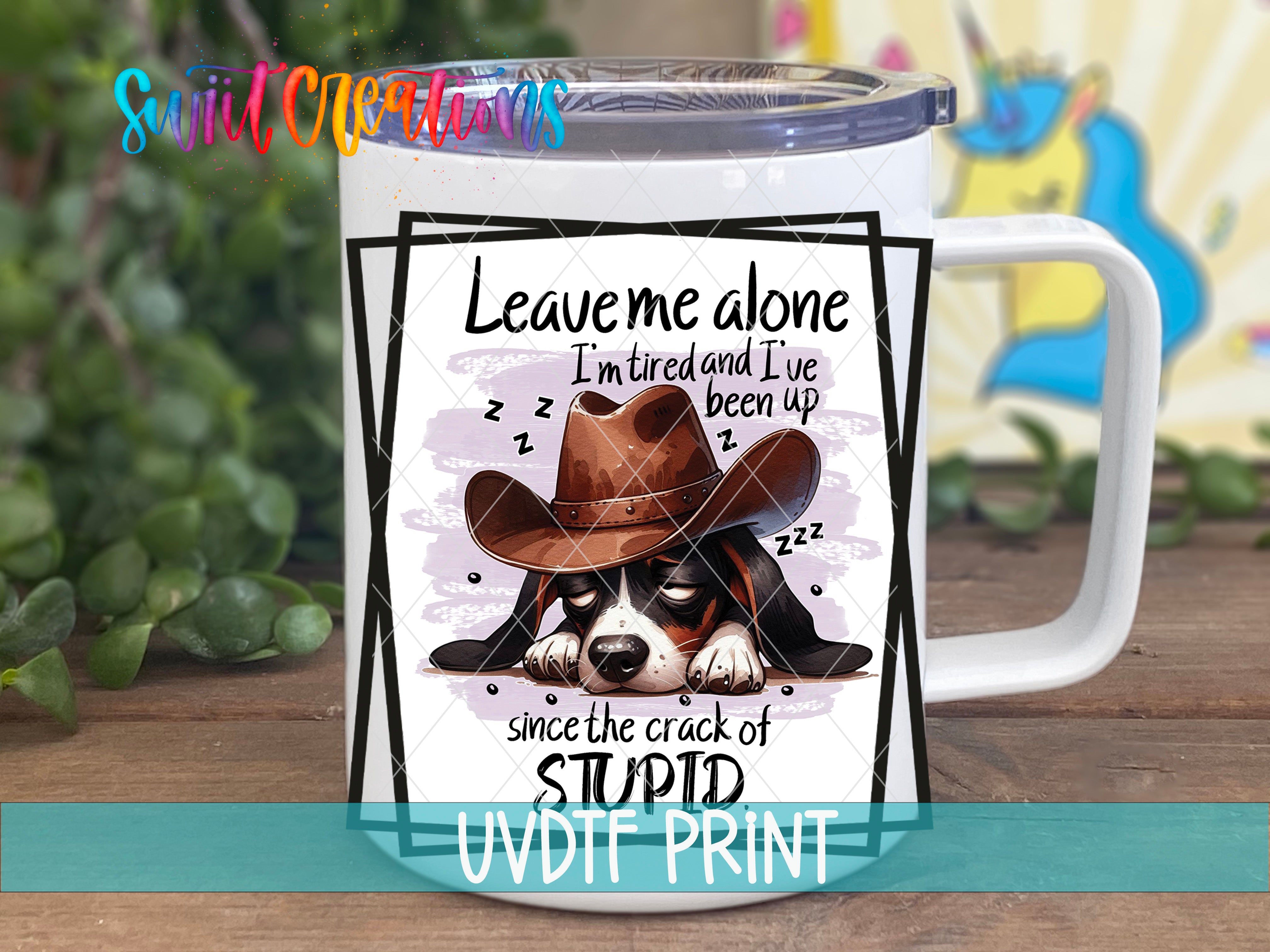 A mug with a cartoon image of a dog wearing a cowboy hat and sleeping, accompanied by text that reads "Leave me alone I'm tired and I've been up since the crack of stupid UVDF PRINT".