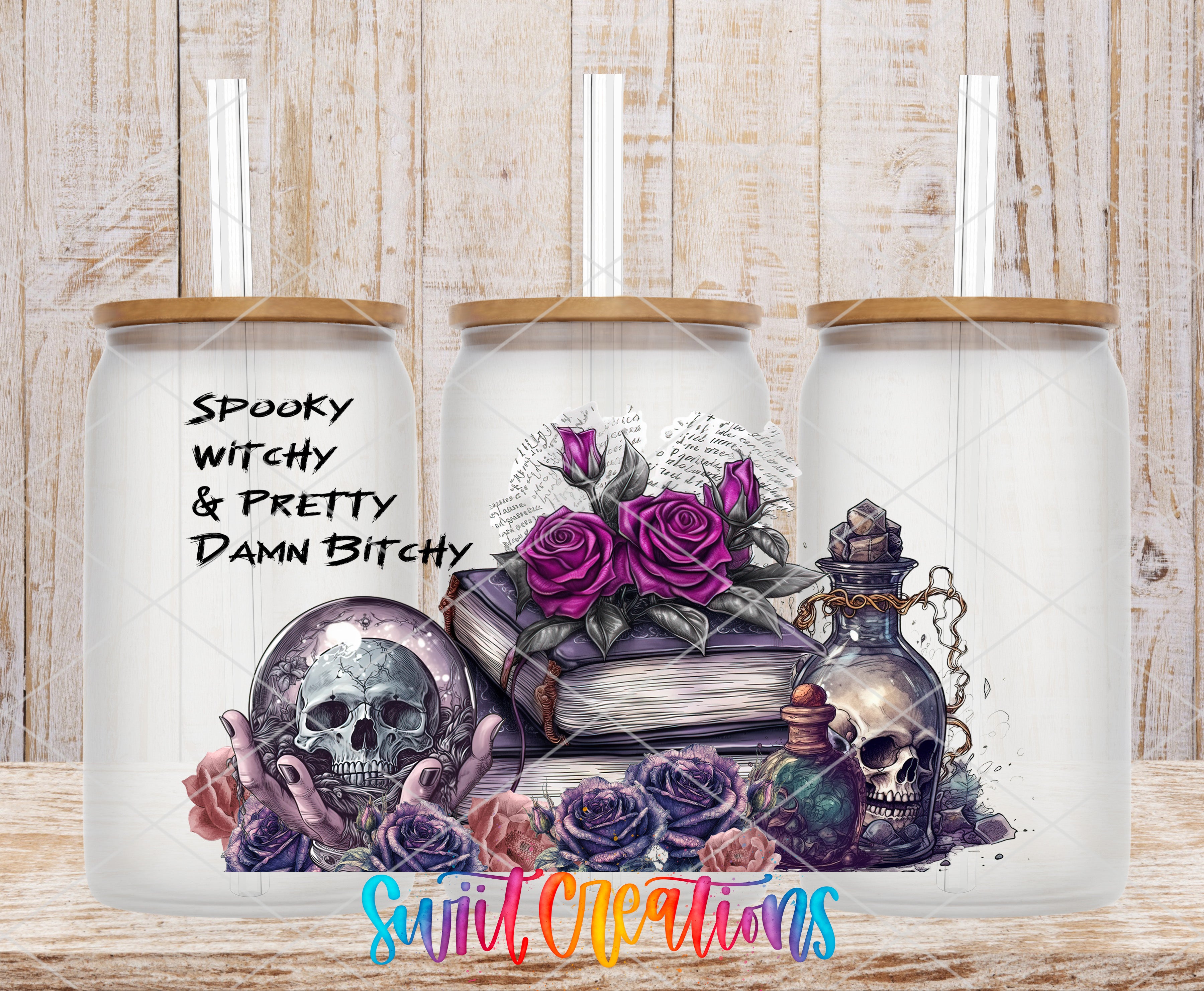 A trio of glass jars with spooky and pretty designs, including skulls, roses, and other elements, set against a wooden background.
