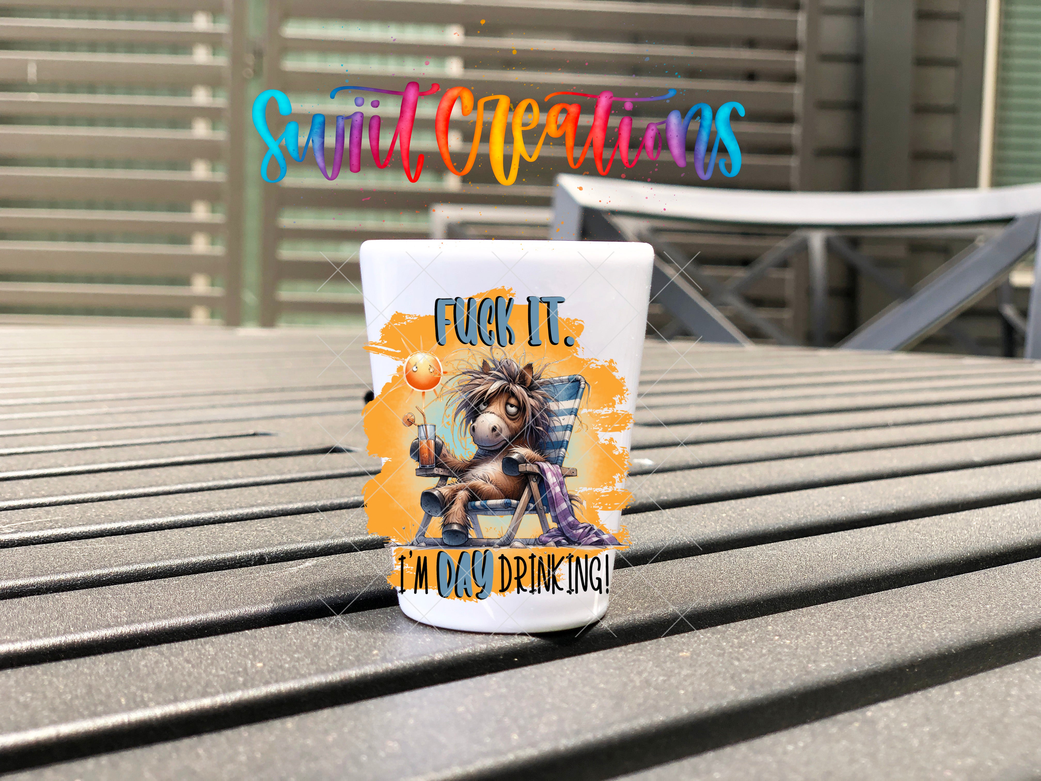 A mug with a cartoon horse and the text "FUCK IT! I'M DAY DRINKING!" printed on it, placed on a wooden surface.