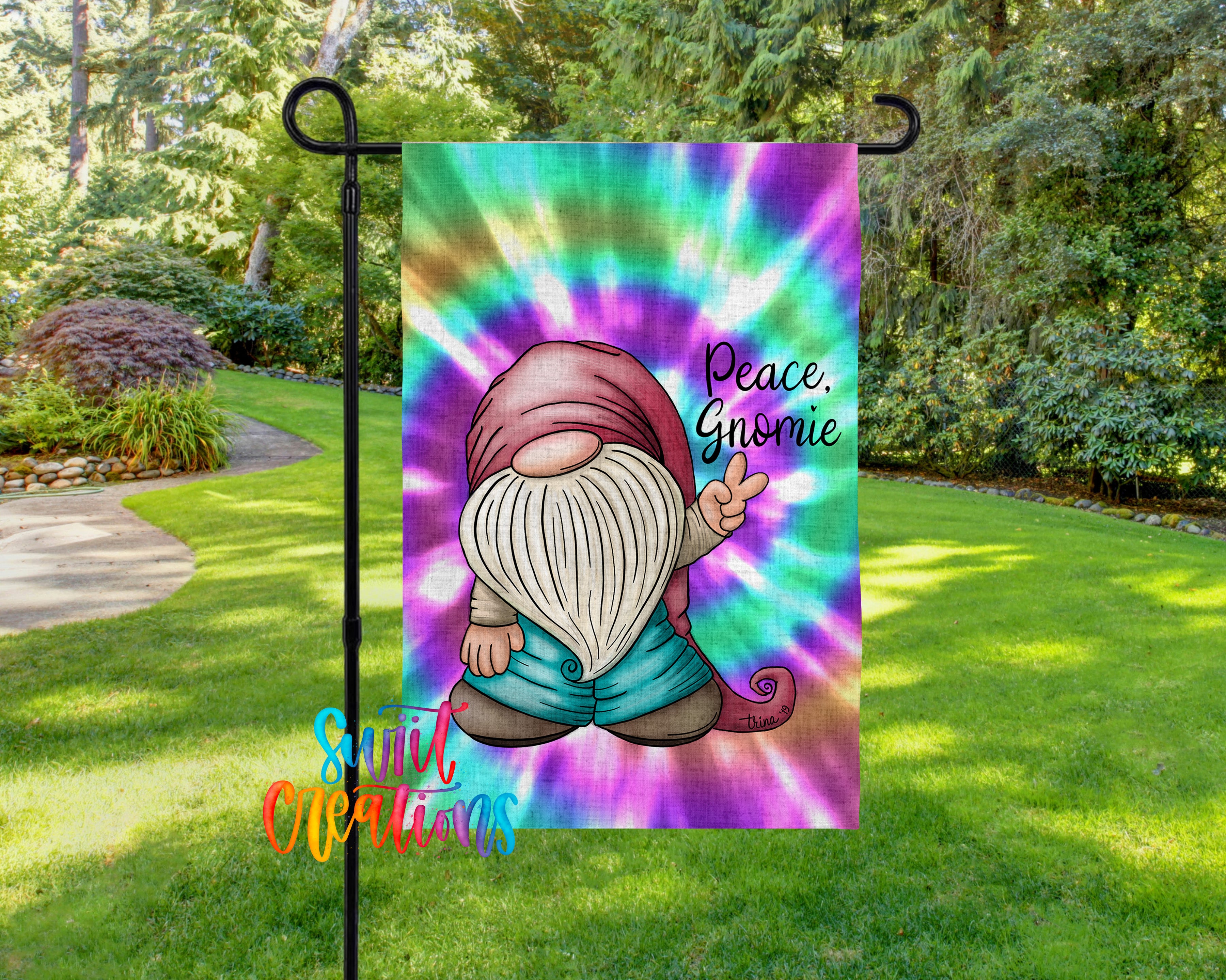 A colorful garden gnome flag with a peace sign and the text "Peace. Gnome" is displayed in a grassy area surrounded by trees.