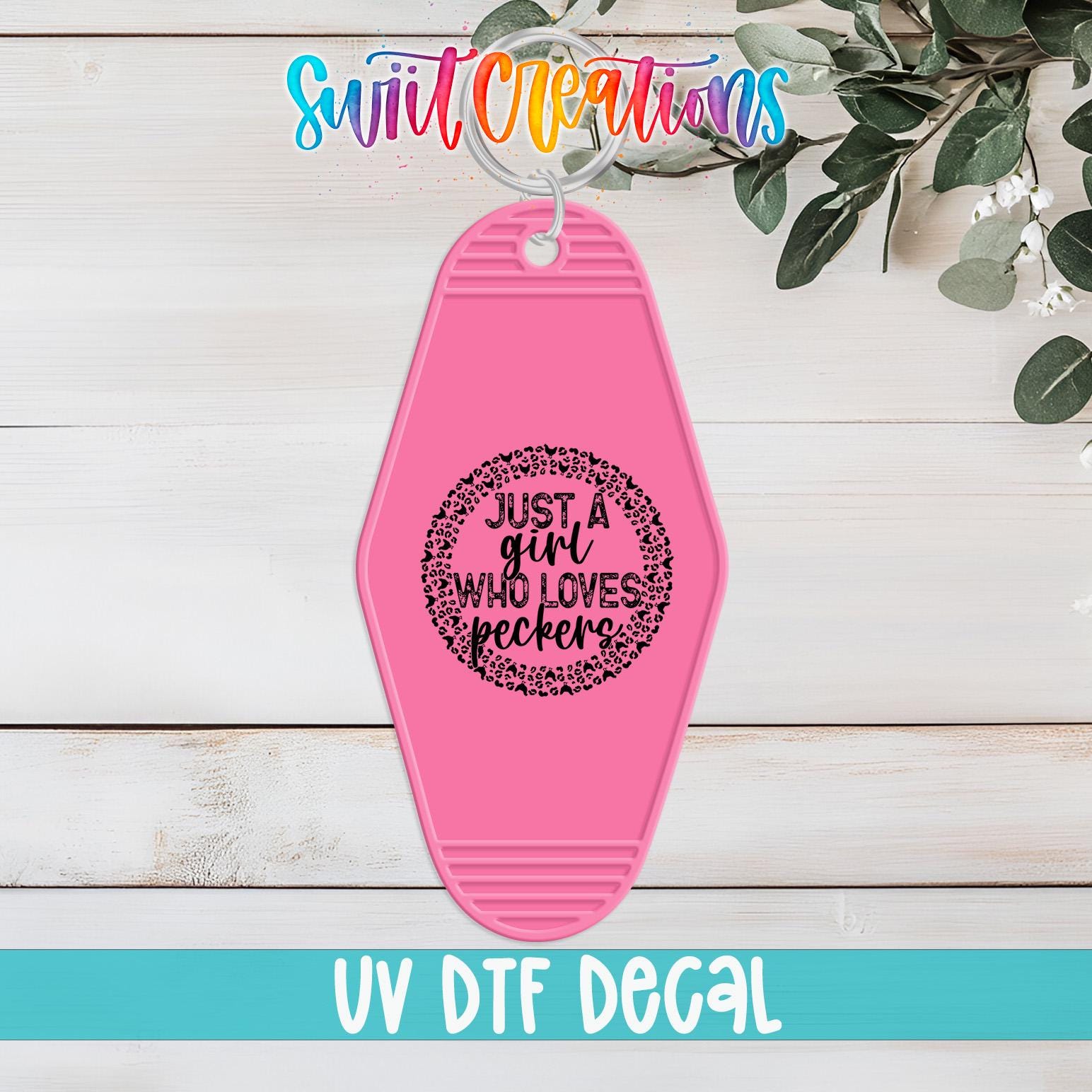 A pink keychain with a black text design that says "Just a girl who loves peckers" is displayed on a wooden surface.
