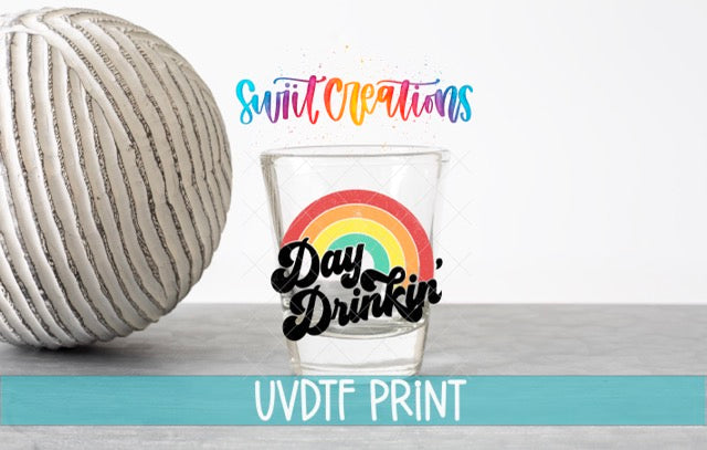 a glass with a rainbow design and the text "Day Drinkin'" on it, along with a ball and a rainbow graphic. The text "Swit Creations" is written above the glass, and "UVDF PRINT" is written below the glass.