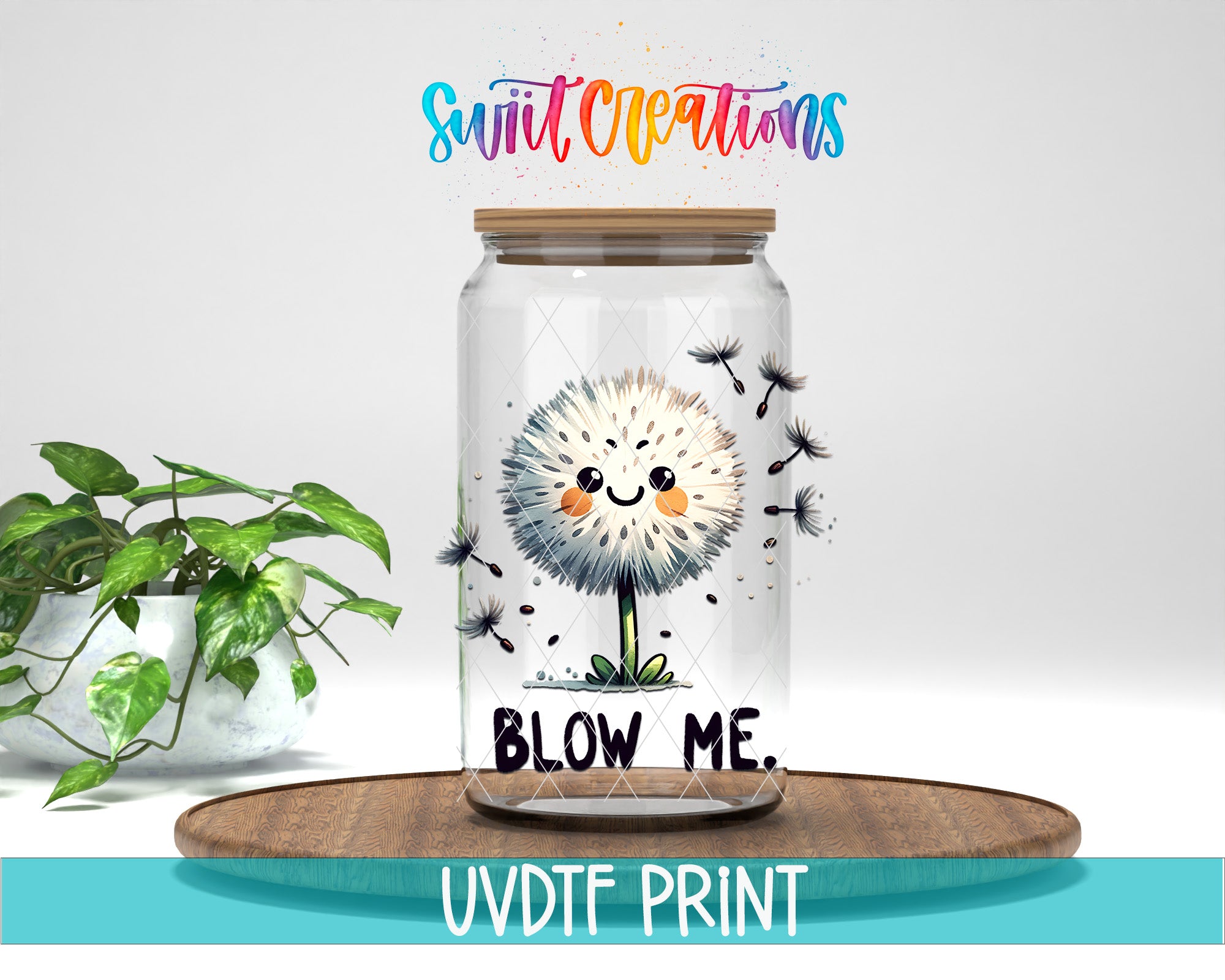 A glass jar with a smiling dandelion flower design and the text "BLOW ME" inside, placed on a wooden surface next to a potted plant.
