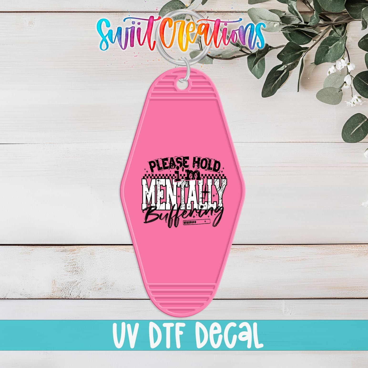 A pink keychain with a humorous text message printed on it, placed on a wooden surface with some greenery in the background.