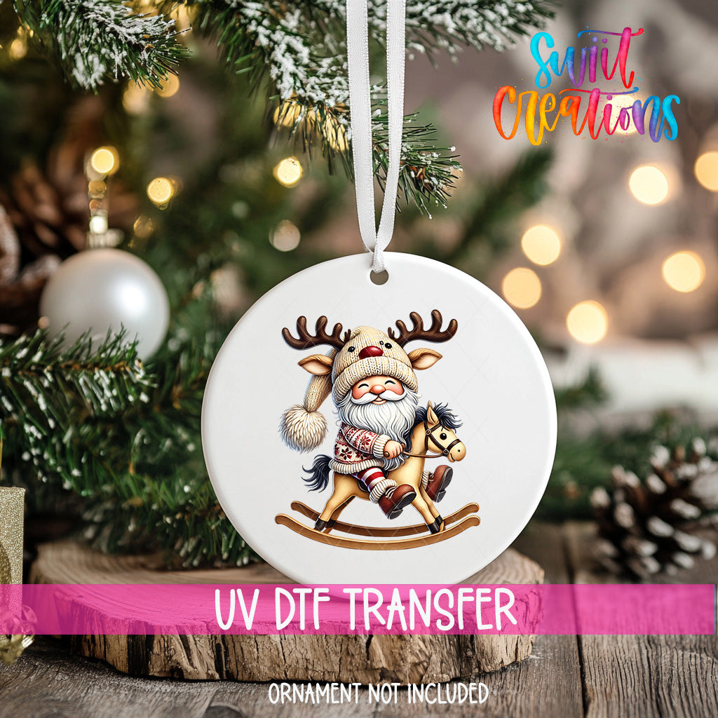A white ornament with a Santa Claus figure riding a rocking horse is hanging on a Christmas tree.