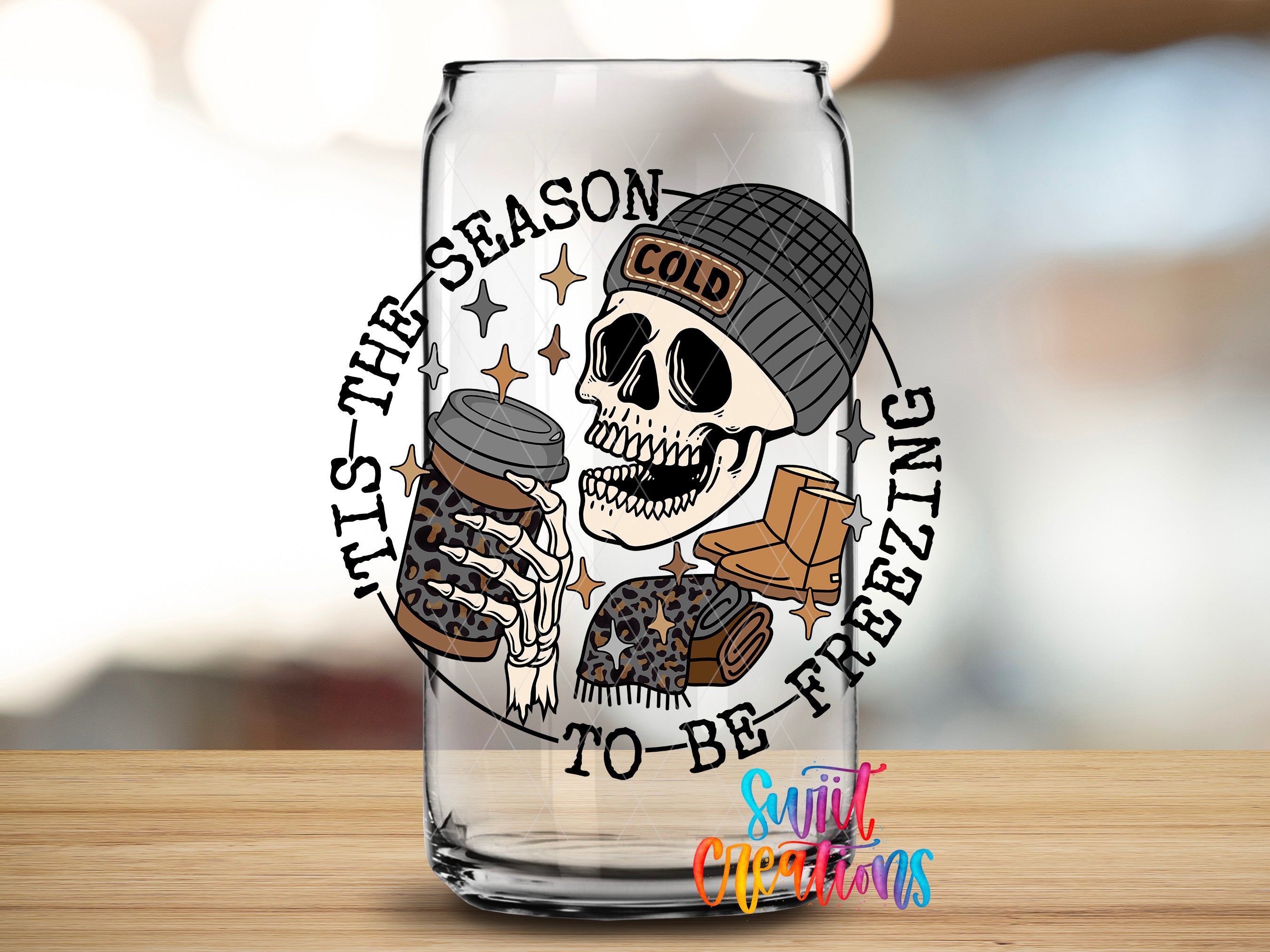 A glass with a skull wearing a beanie and holding a coffee cup, surrounded by the text "It's the season to be freezing" and "To be freezing".