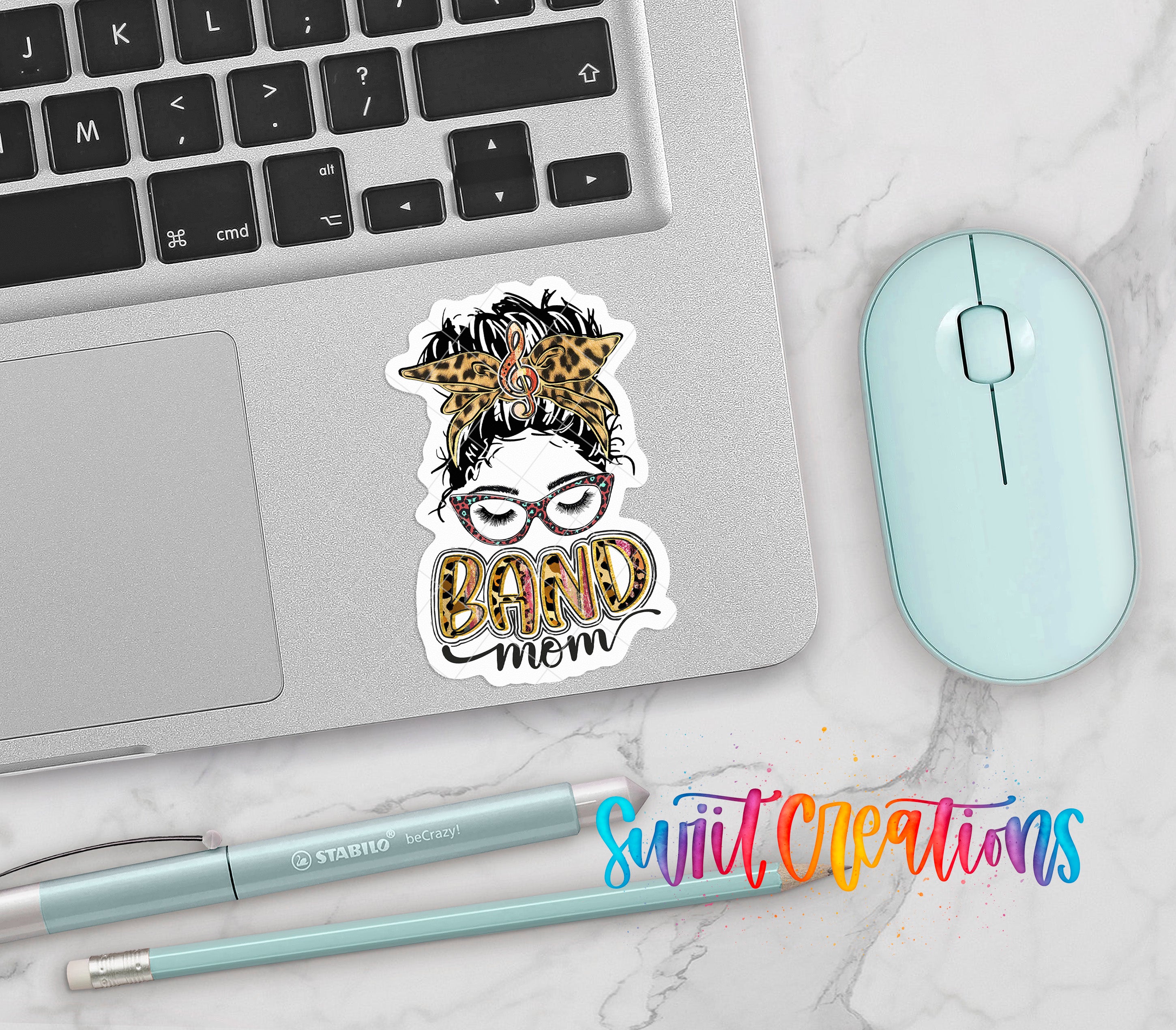 a laptop with a sticker that says "BAD MOM", a mouse, a pen, and a pencil on a marble surface.