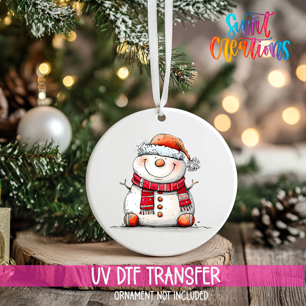 A white ornament with a snowman design hangs on a Christmas tree, surrounded by pine branches and twinkling lights.