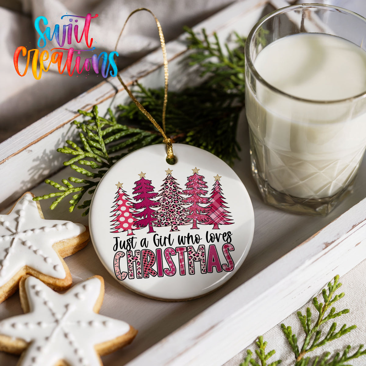 a Christmas ornament with a tree design, a glass of milk, and some cookies on a white surface.