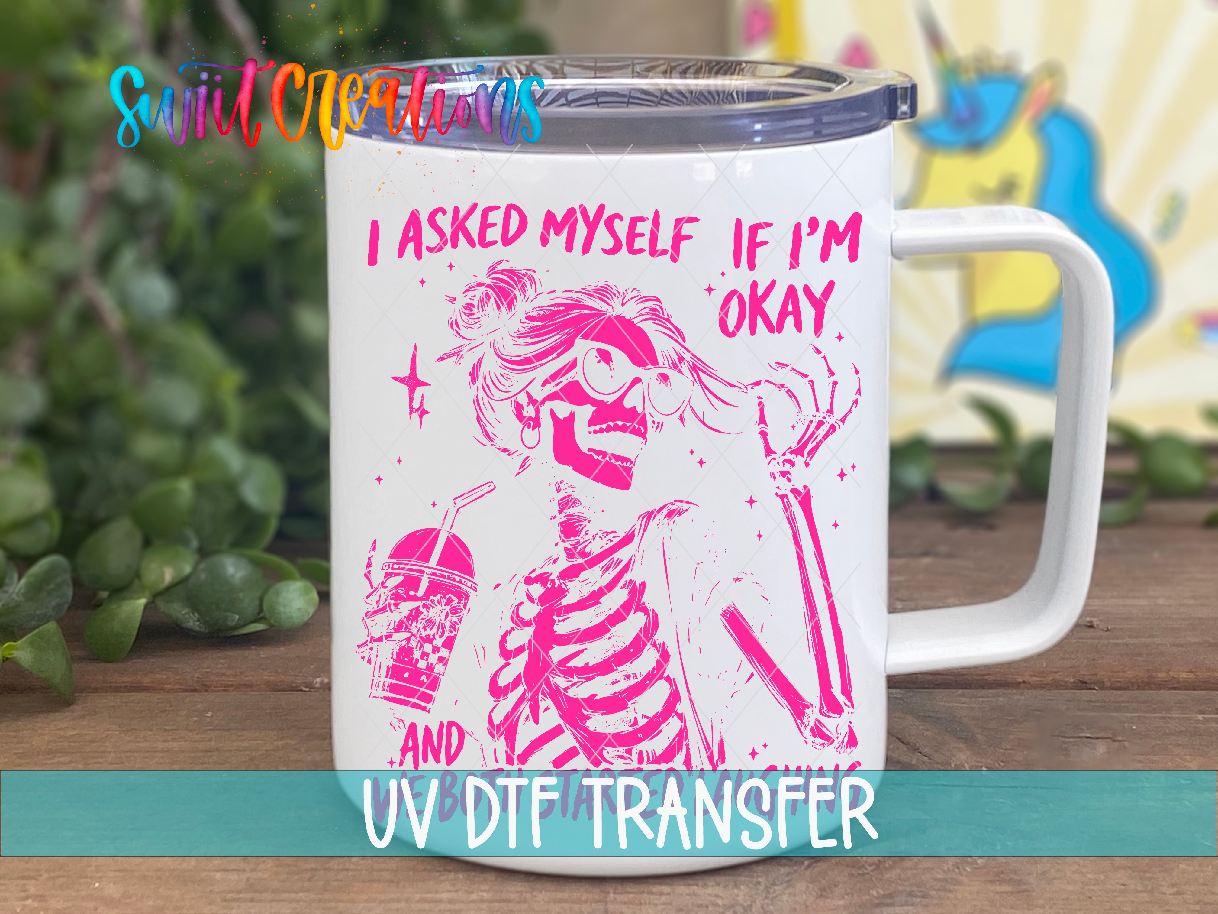 A white mug with a pink skeleton design and text printed on it, placed on a wooden surface.