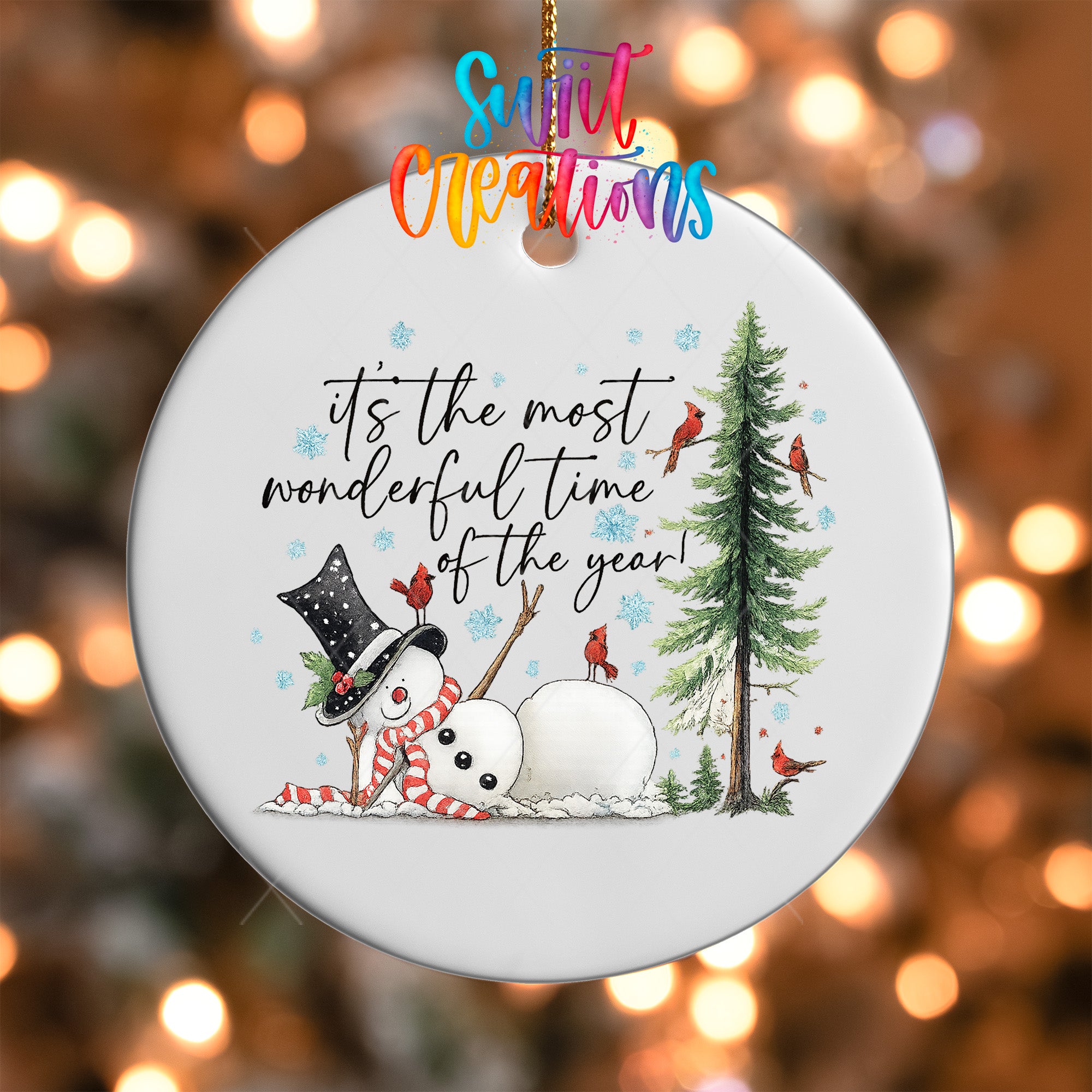 A white ornament with a snowman, a snowman, and a pine tree, along with birds, against a background of colorful lights.