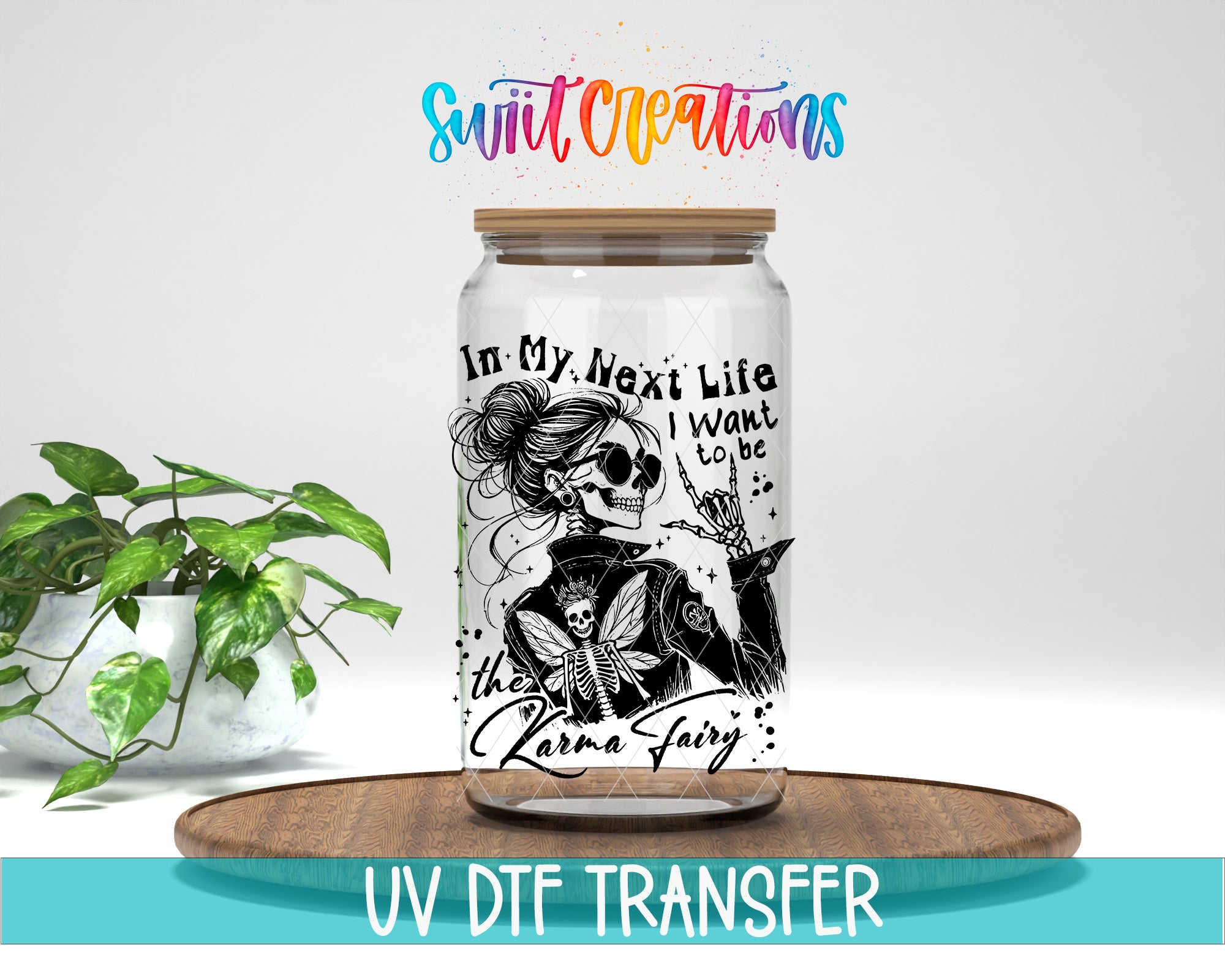 A glass jar with a black and white illustration of a skeleton wearing sunglasses and a skull hat, along with the text "In My Next Life I Want to Be the Karma Fairy". The jar is placed on a wooden tray, and there is a potted plant in the background.