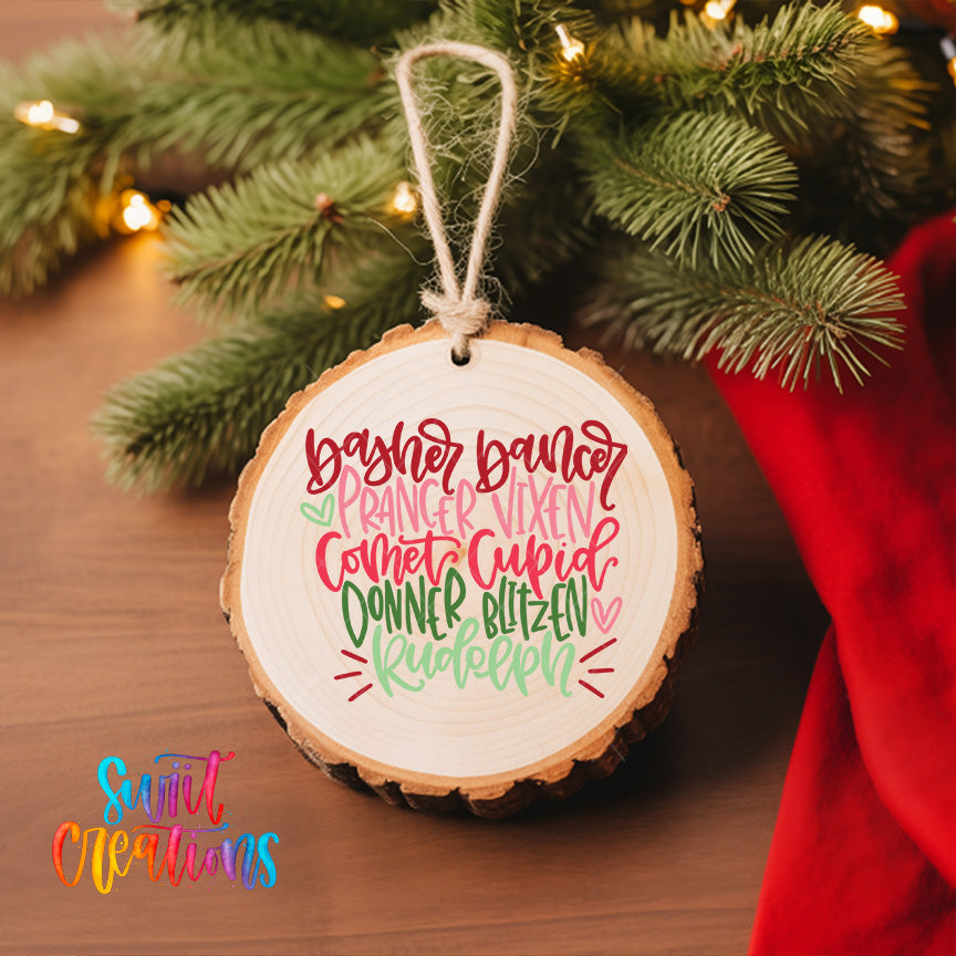 A wooden ornament with a white background and colorful text, hanging on a Christmas tree.