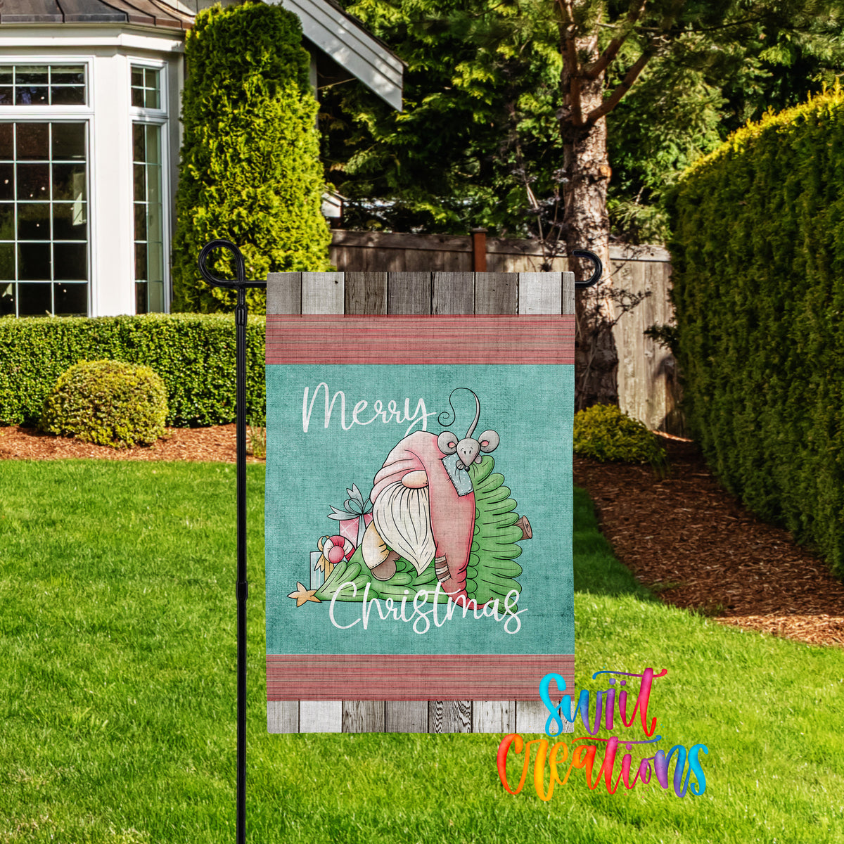 A colorful garden sign with a gnome and Christmas decorations, placed in a grassy yard with a house and trees in the background.