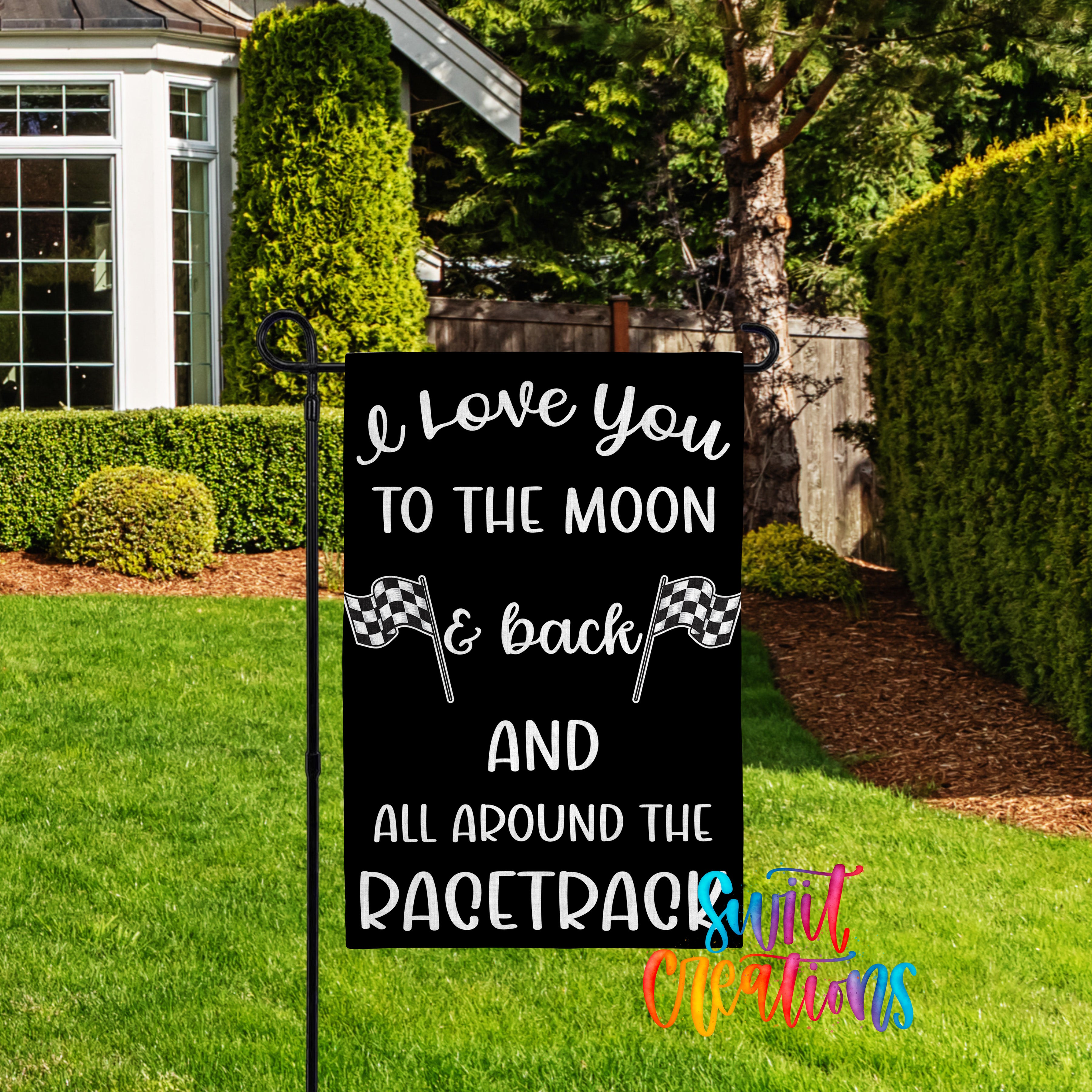 A black sign with white text that reads "I love you to the moon & back and all around the racetrack" is displayed in a grassy yard with a house and trees in the background.