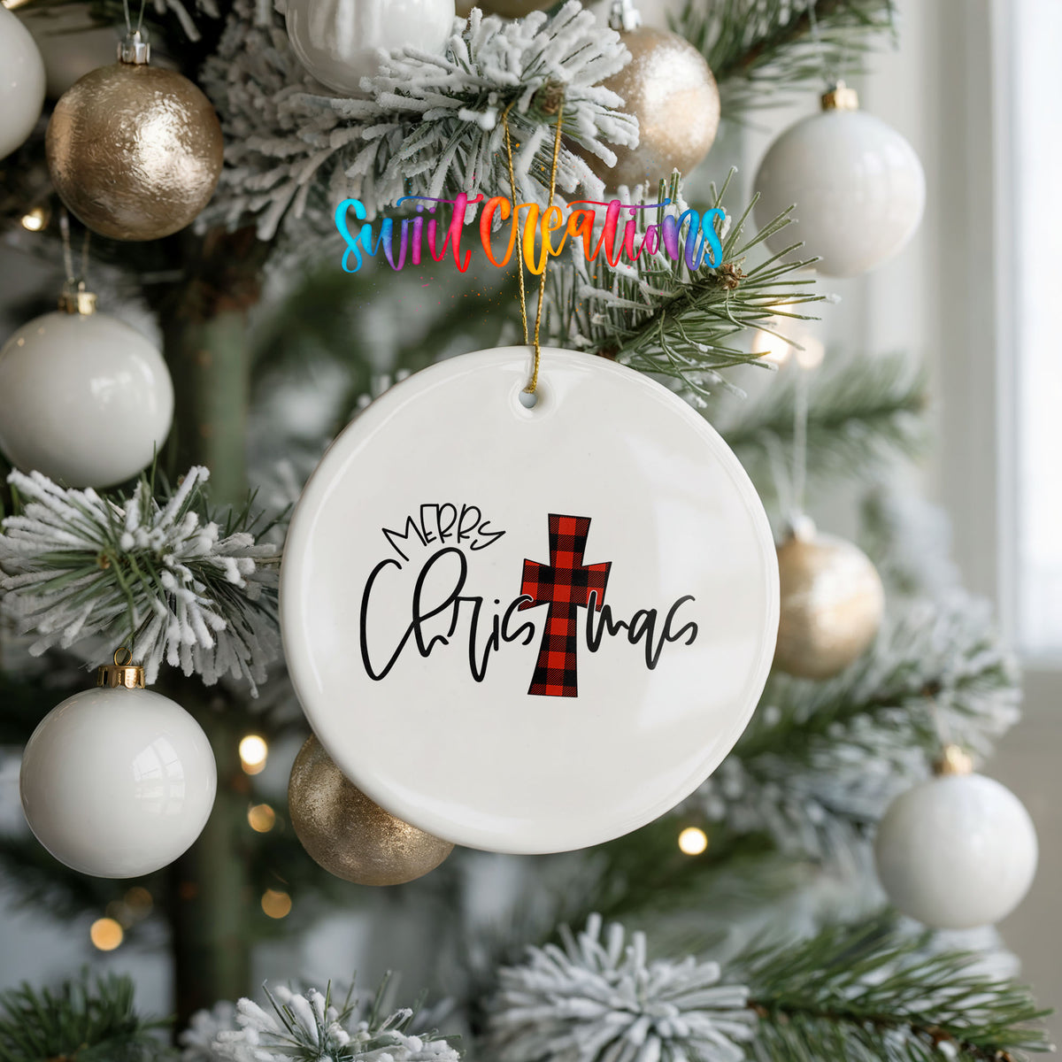 A white Christmas ornament with a red and black plaid cross design hangs on a decorated tree.