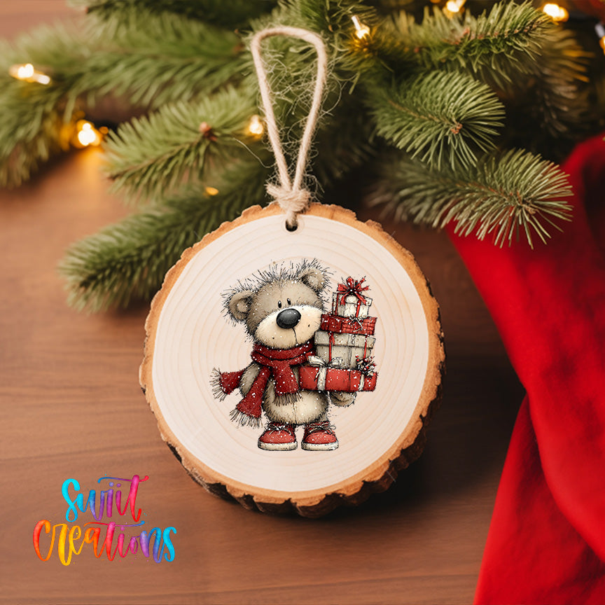 A wooden ornament featuring a teddy bear holding a gift, hanging on a Christmas tree with a red cloth visible in the background.