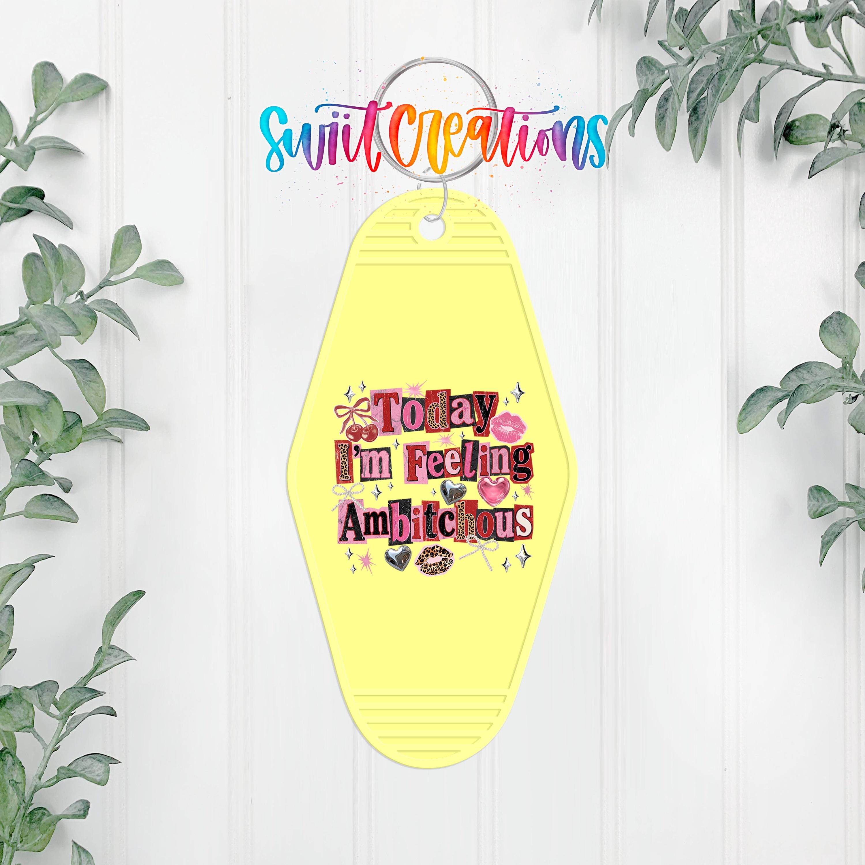 A yellow keychain with a colorful, whimsical design hanging on a white wall, surrounded by greenery.