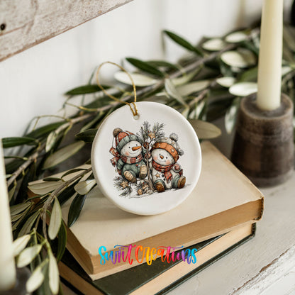 A ceramic ornament featuring two snowmen is placed on top of a stack of books, surrounded by greenery.