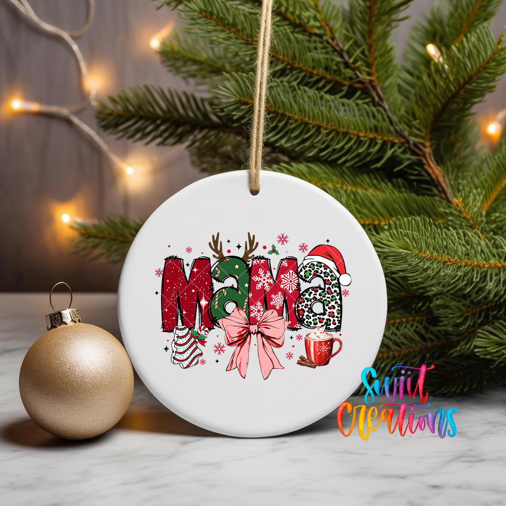 A white ceramic ornament with the word "Mama" written on it, surrounded by Christmas decorations such as snowflakes, reindeer, and a mug. The ornament is hanging from a string, and there is a gold ornament next to it on a marble surface.