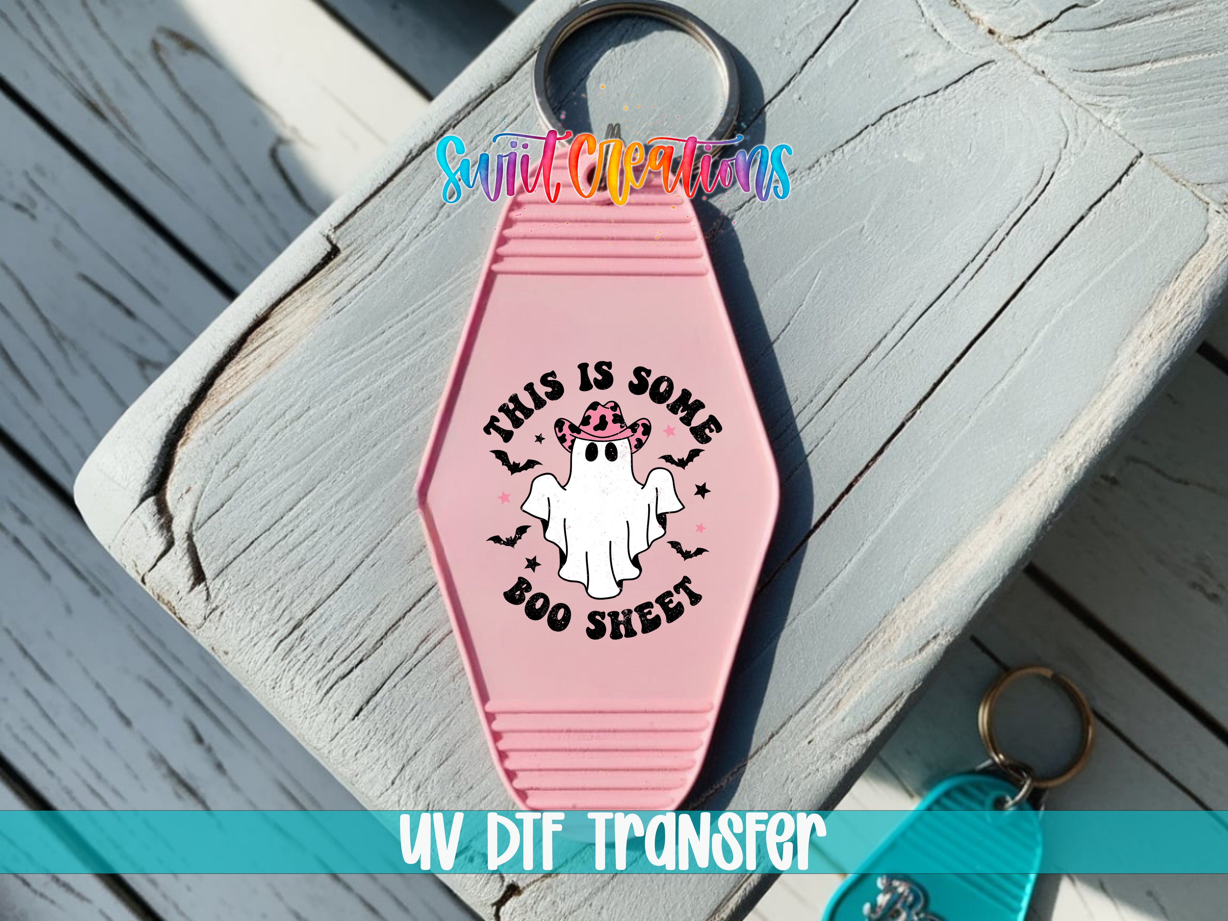 A pink keychain with a ghost design and text, placed on a wooden surface.