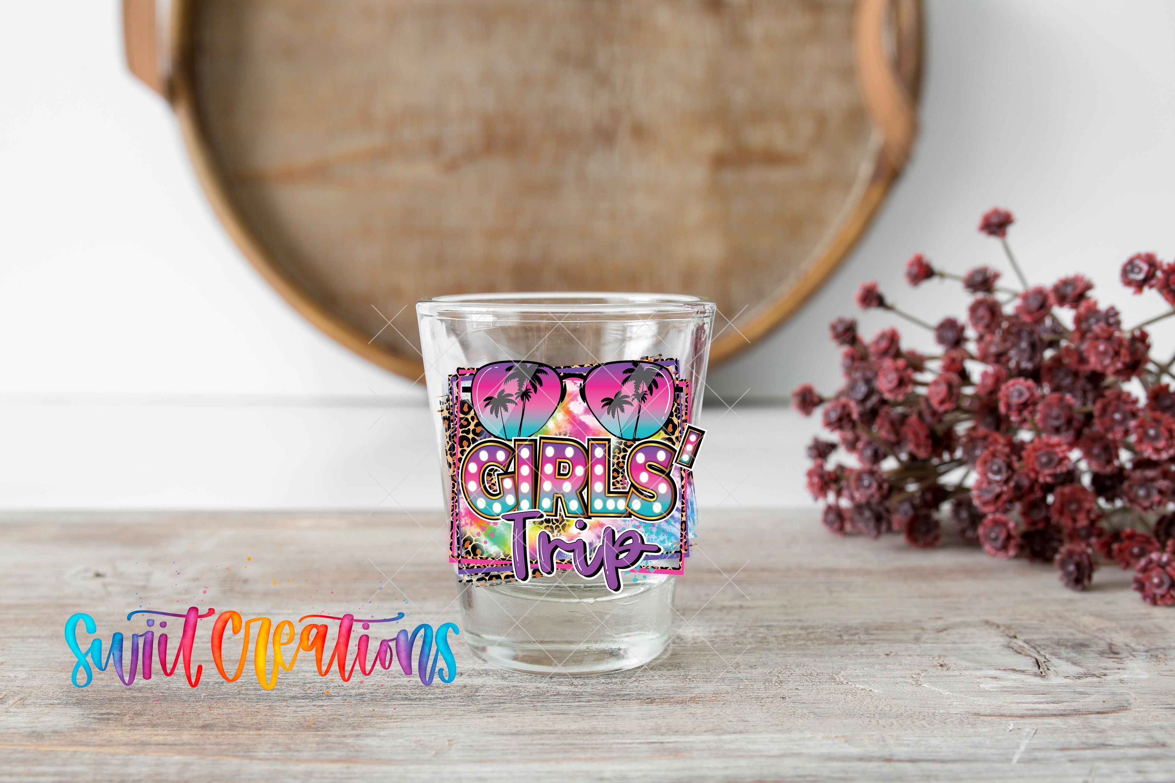 A clear glass with a colorful graphic design on it, placed on a wooden surface next to a bunch of red flowers.