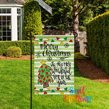 A festive Christmas-themed garden sign with a colorful design and text, placed in a well-maintained yard with a house and trees in the background.