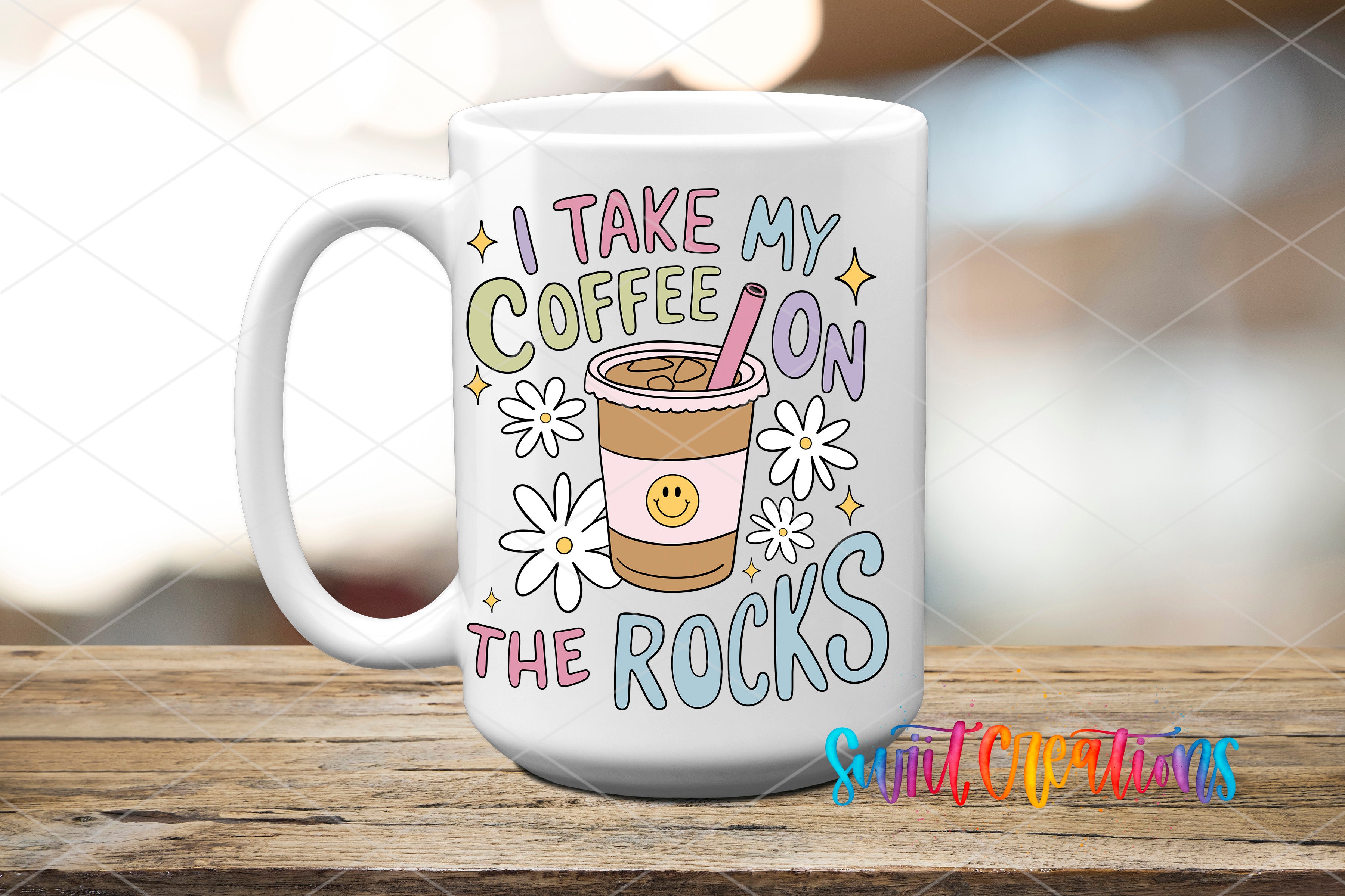 A white coffee mug with a colorful design featuring a coffee cup with a smiley face, flowers, and the text "I TAKE MY COFFEE ON THE ROCKS" printed on it.