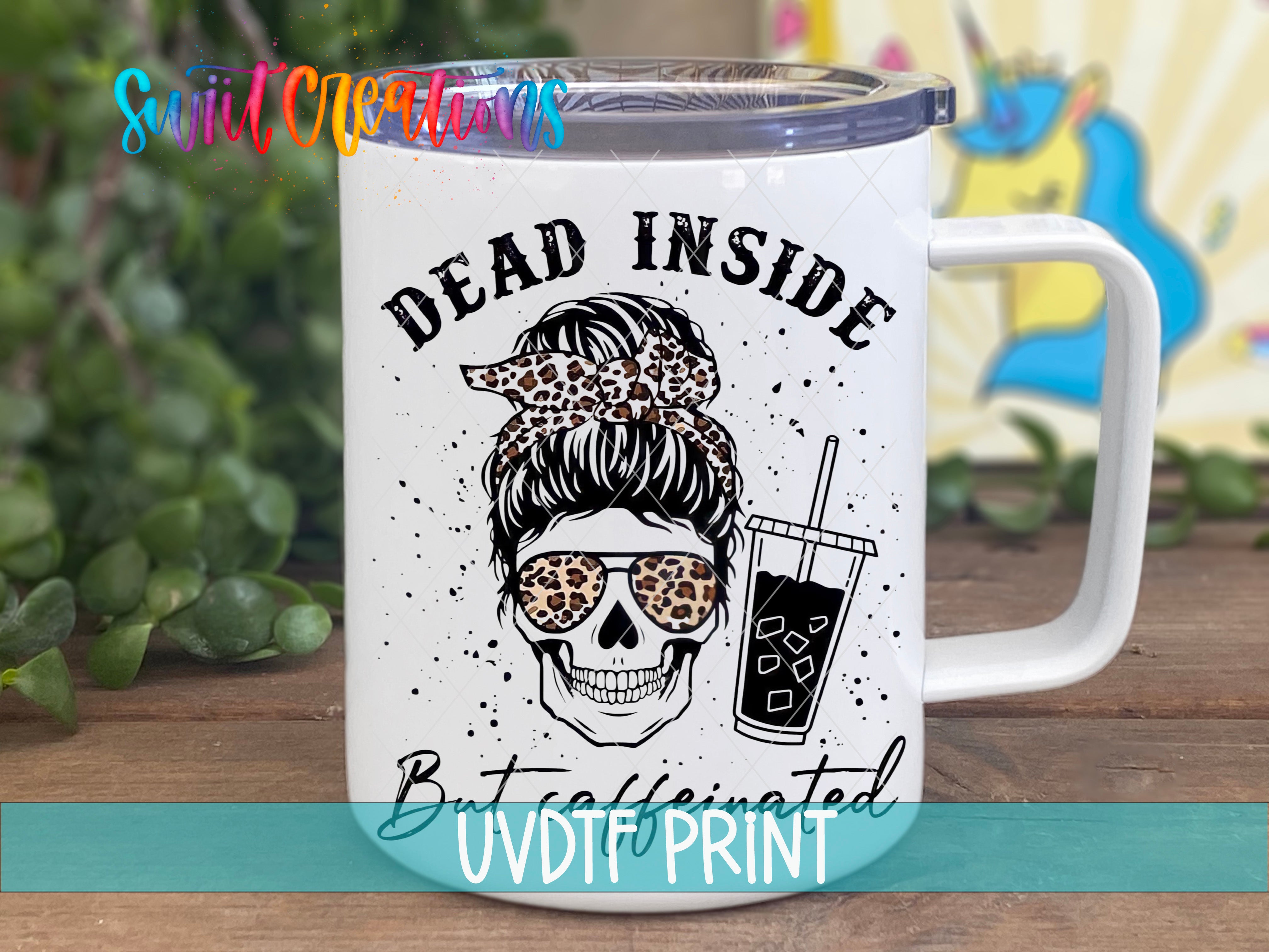 A white mug with a black and white skull design and the text "Dead inside" printed on it, along with a drink in a cup.