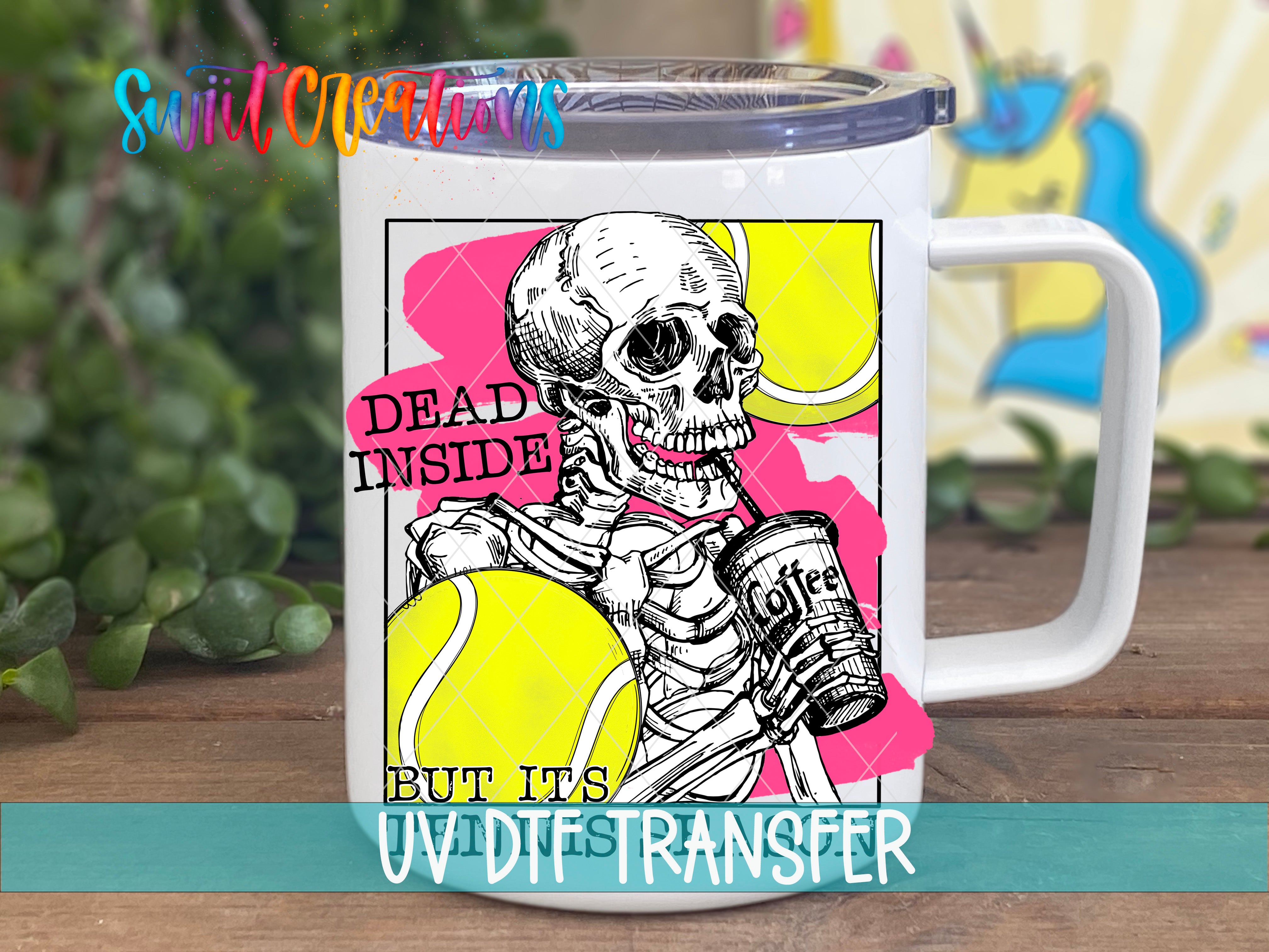A white mug with a colorful illustration of a skeleton holding a can of coffee and a tennis ball, accompanied by the text "Dead inside but it's UV die transfer".