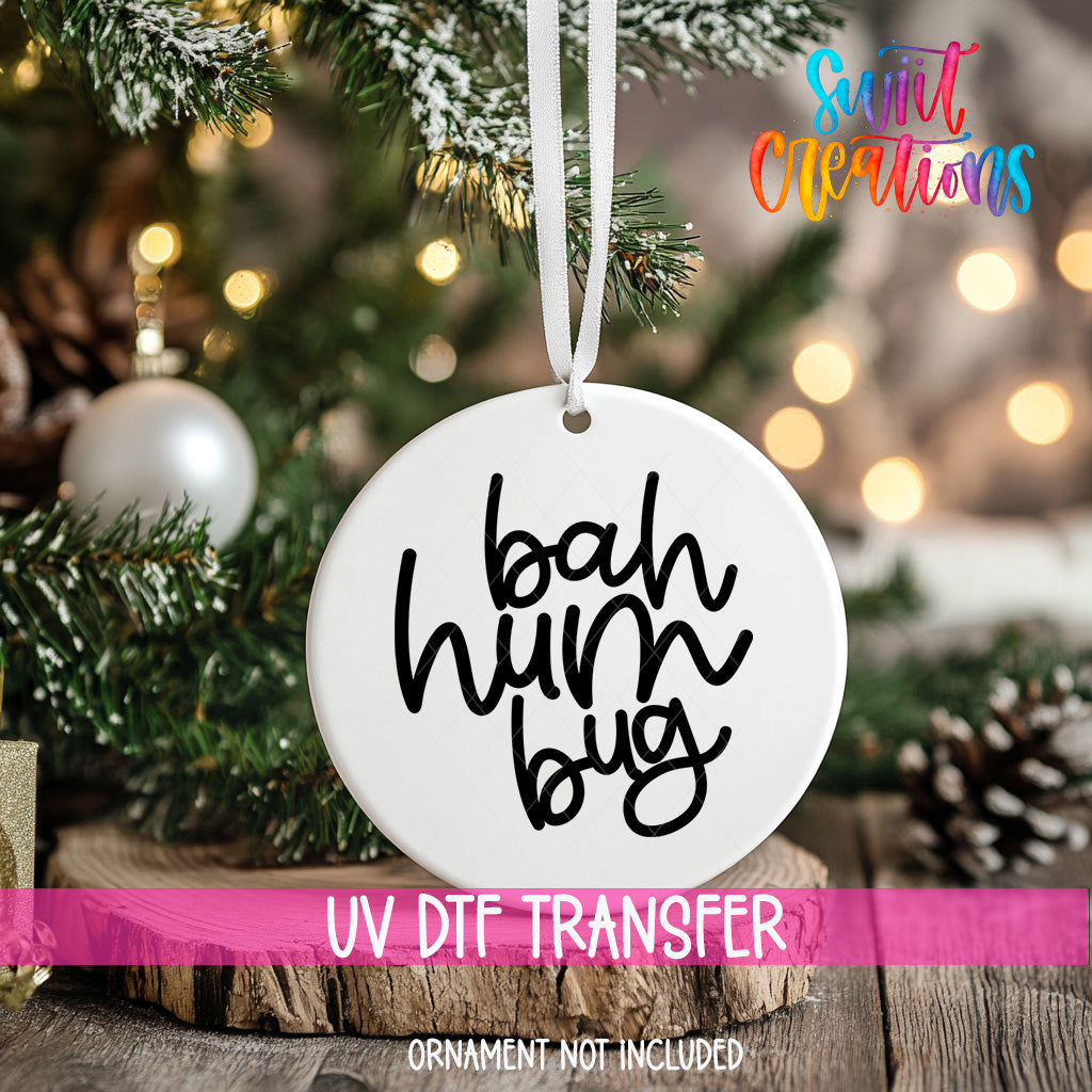 A white ornament with the text "bah hum bug" hanging on a Christmas tree.