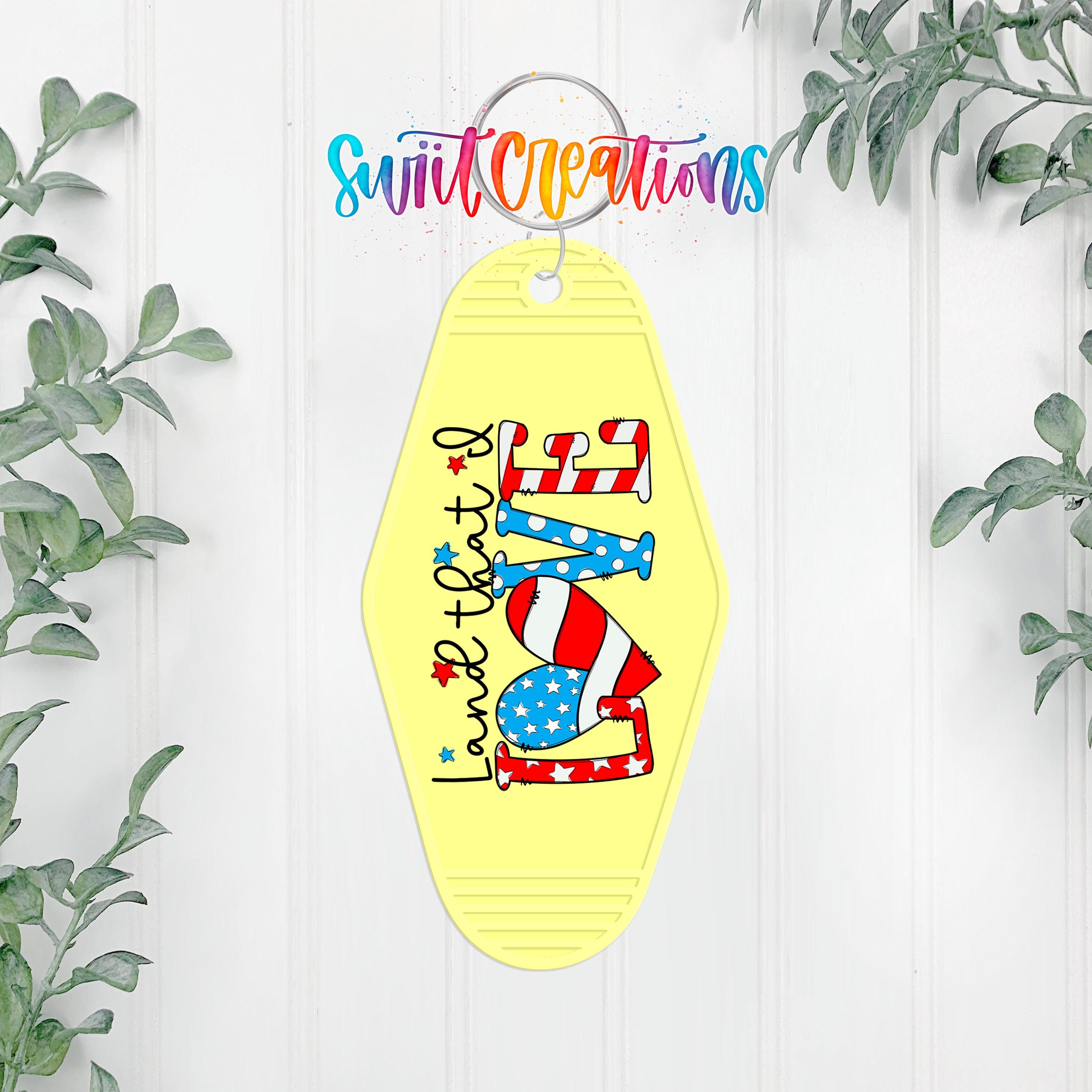 A yellow keychain with a patriotic design, featuring a heart and stars, hangs on a white wall.