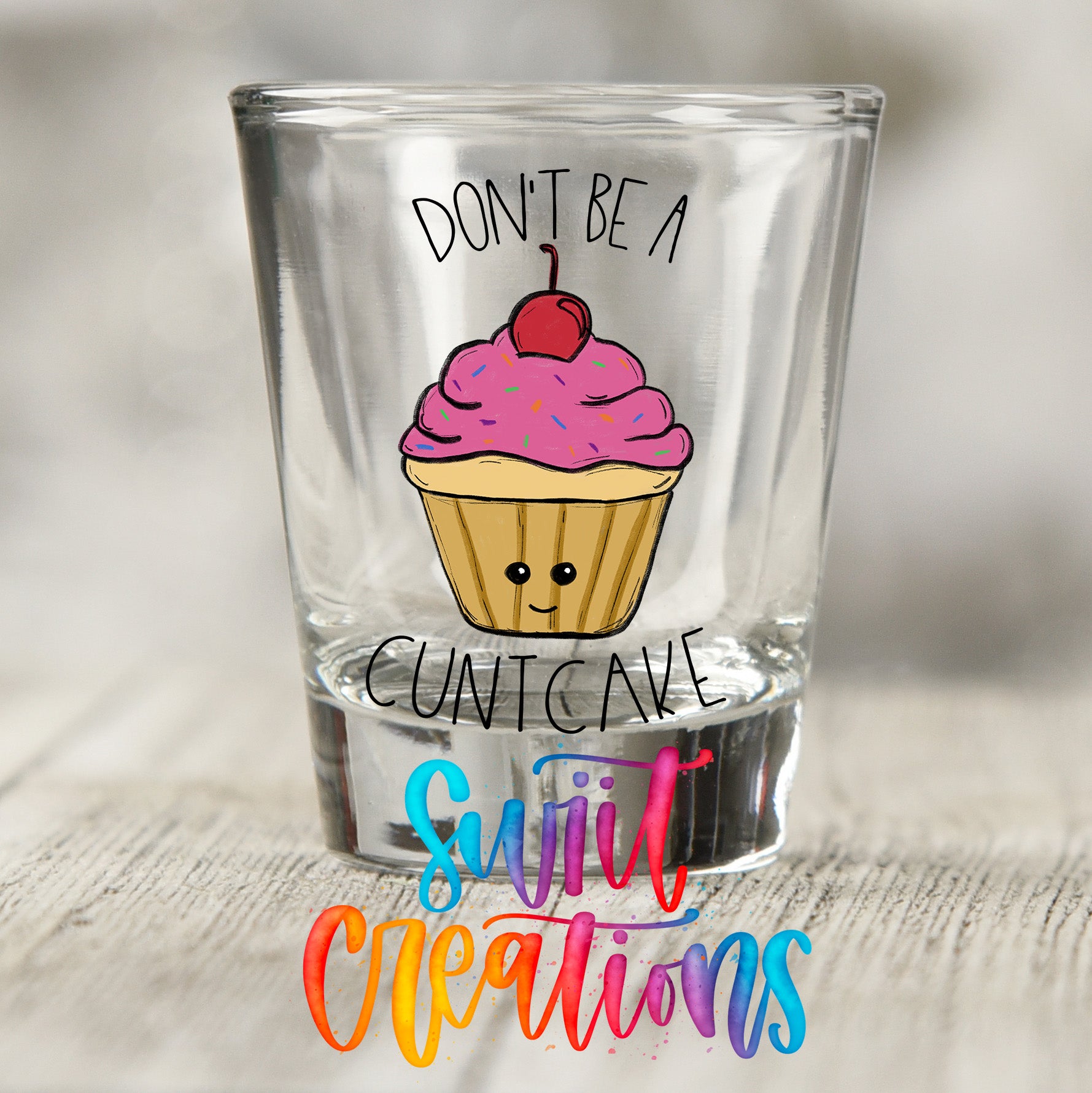 A shot glass with a cupcake design and the text "DON'T BE A CUNTCAKE" printed on it.