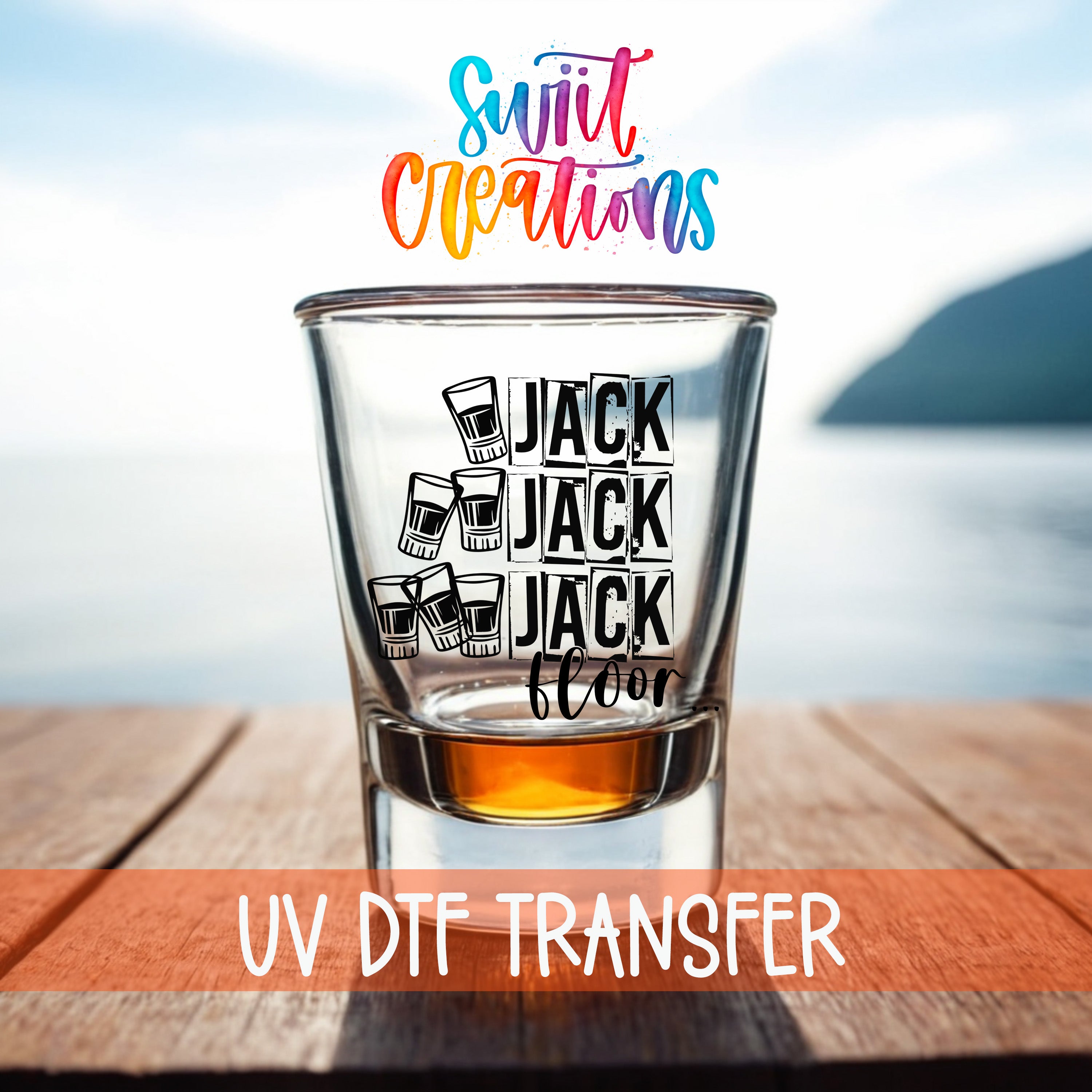 A shot glass with the text "JACK JACK FLOOR" printed on it, placed on a wooden surface with a body of water in the background.