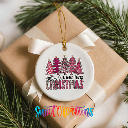 A white ceramic ornament with a Christmas tree design hangs on a brown gift box, surrounded by pine branches.