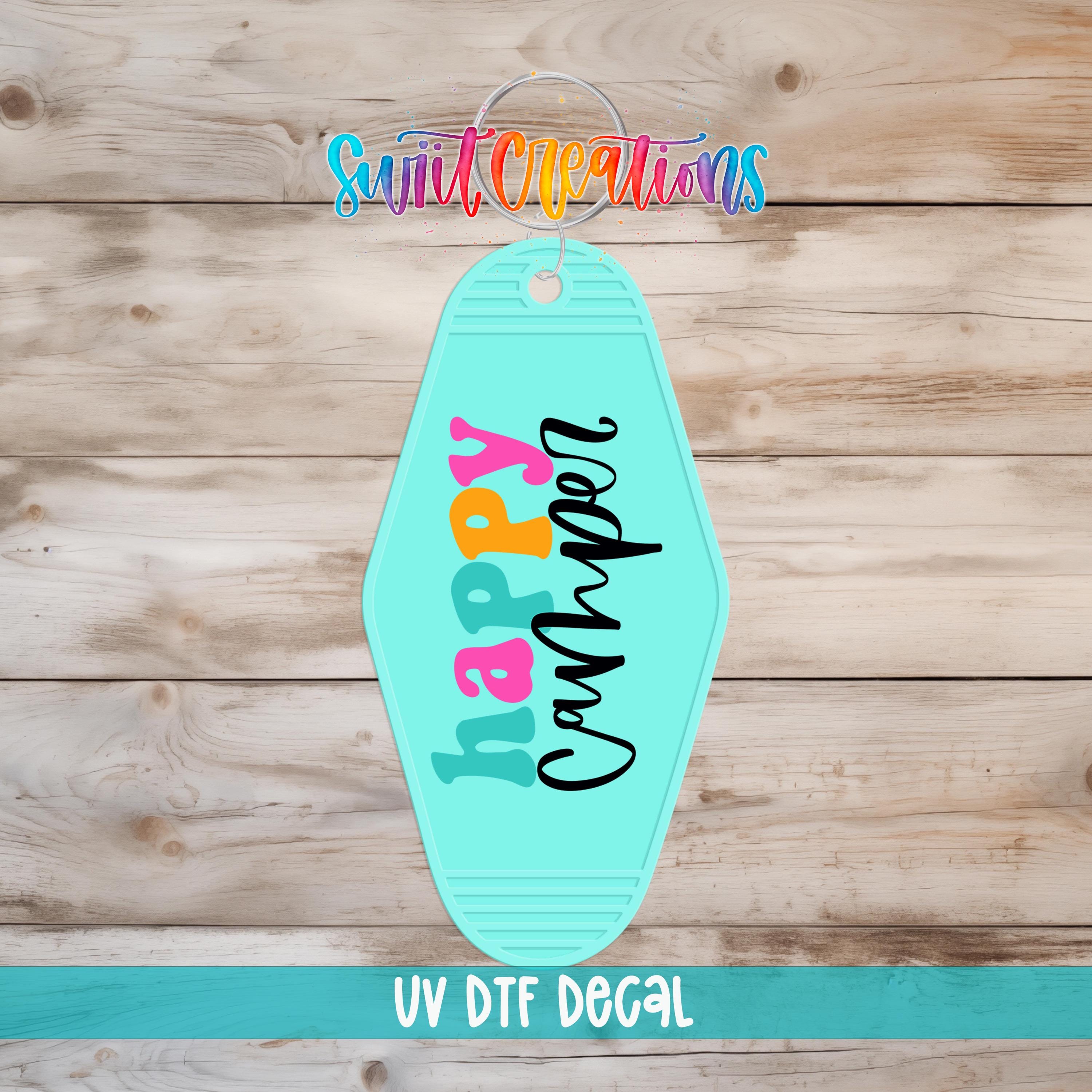 A turquoise keychain with the text "hAPPY" printed on it, displayed on a wooden surface.