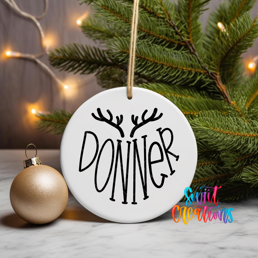 A white ornament with the word "DONNER" written on it, hanging from a string, is placed next to a gold ornament and a Christmas tree.