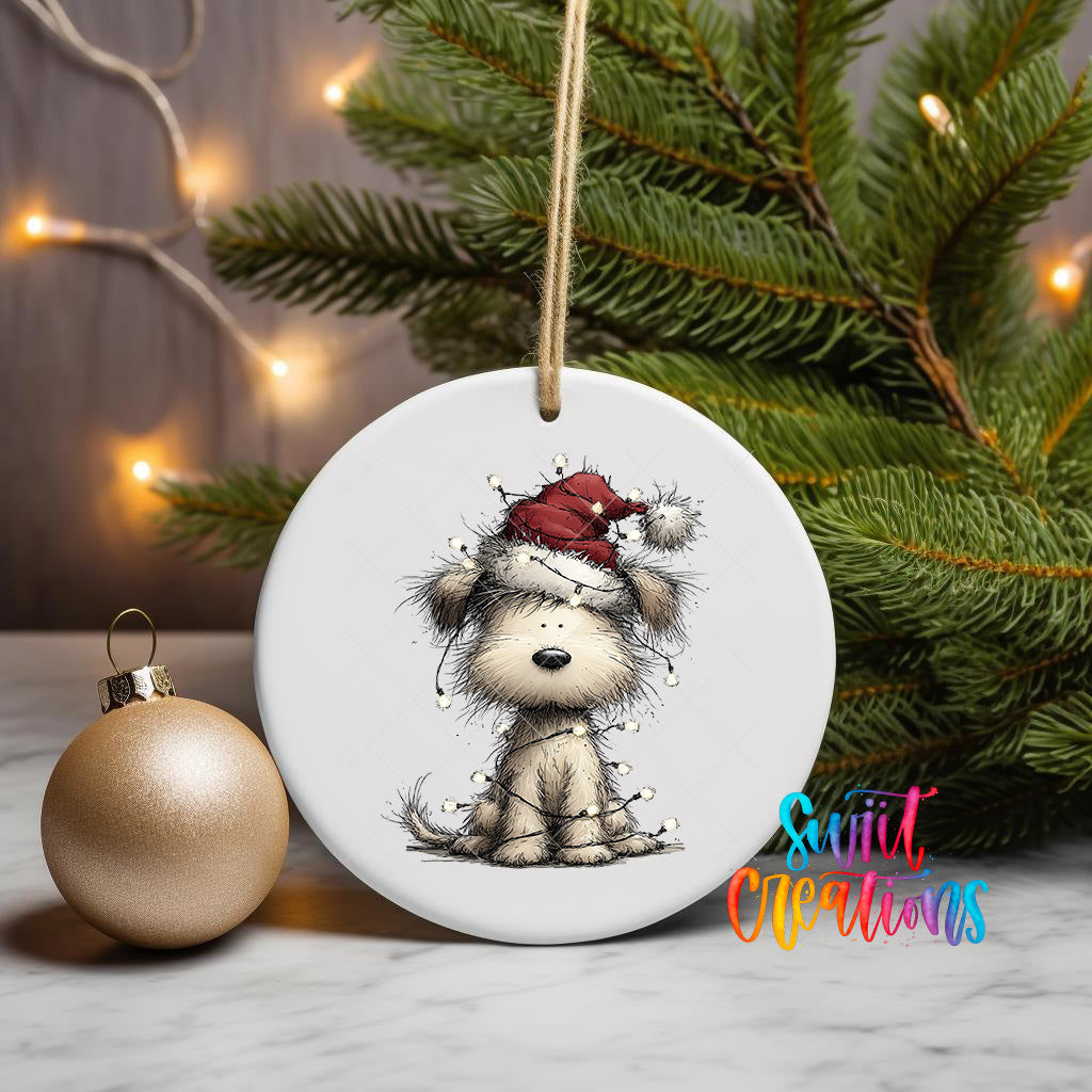 A white ceramic ornament featuring a cartoon image of a dog wearing a Santa hat, hanging on a string next to a gold ornament and a Christmas tree.