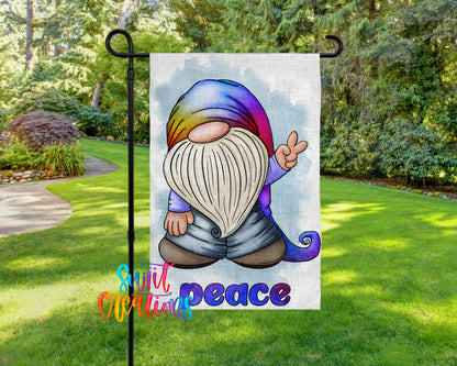 A colorful garden gnome sign with the word "Peace" written below it, set against a backdrop of lush greenery and a winding path.