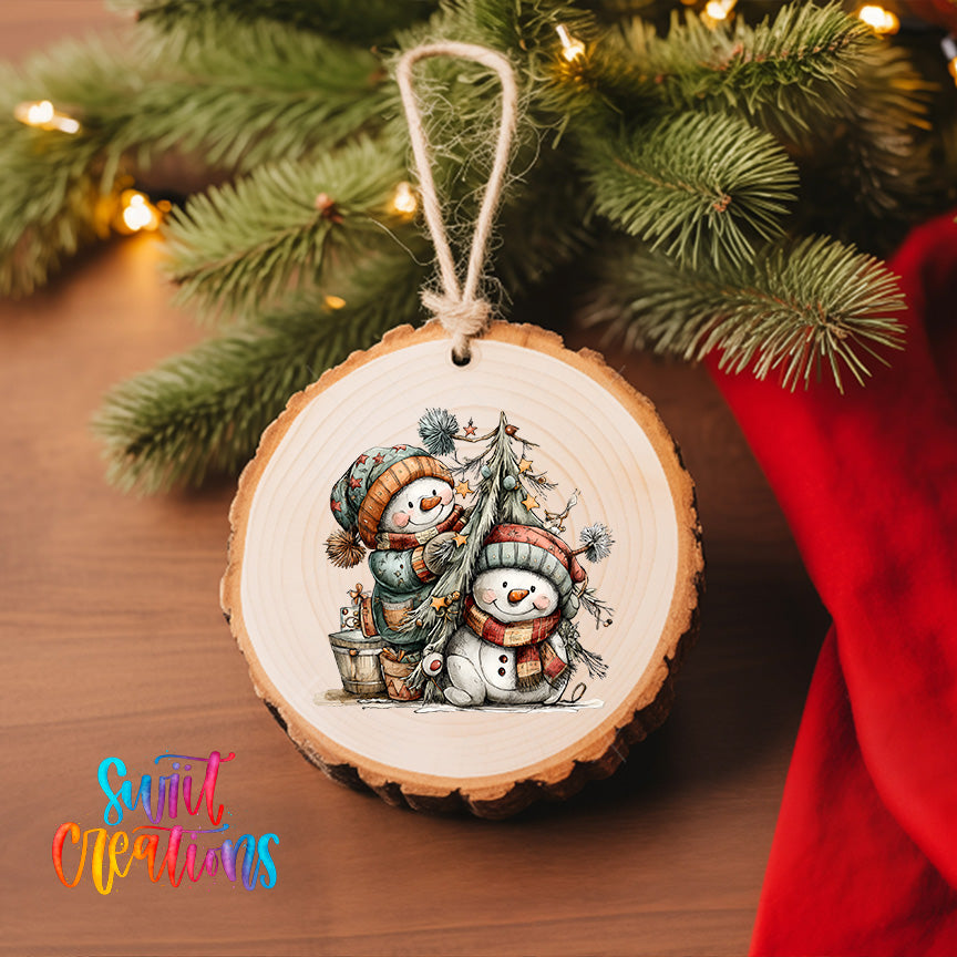 A wooden ornament featuring two snowmen is hanging on a Christmas tree, surrounded by twinkling lights and greenery.